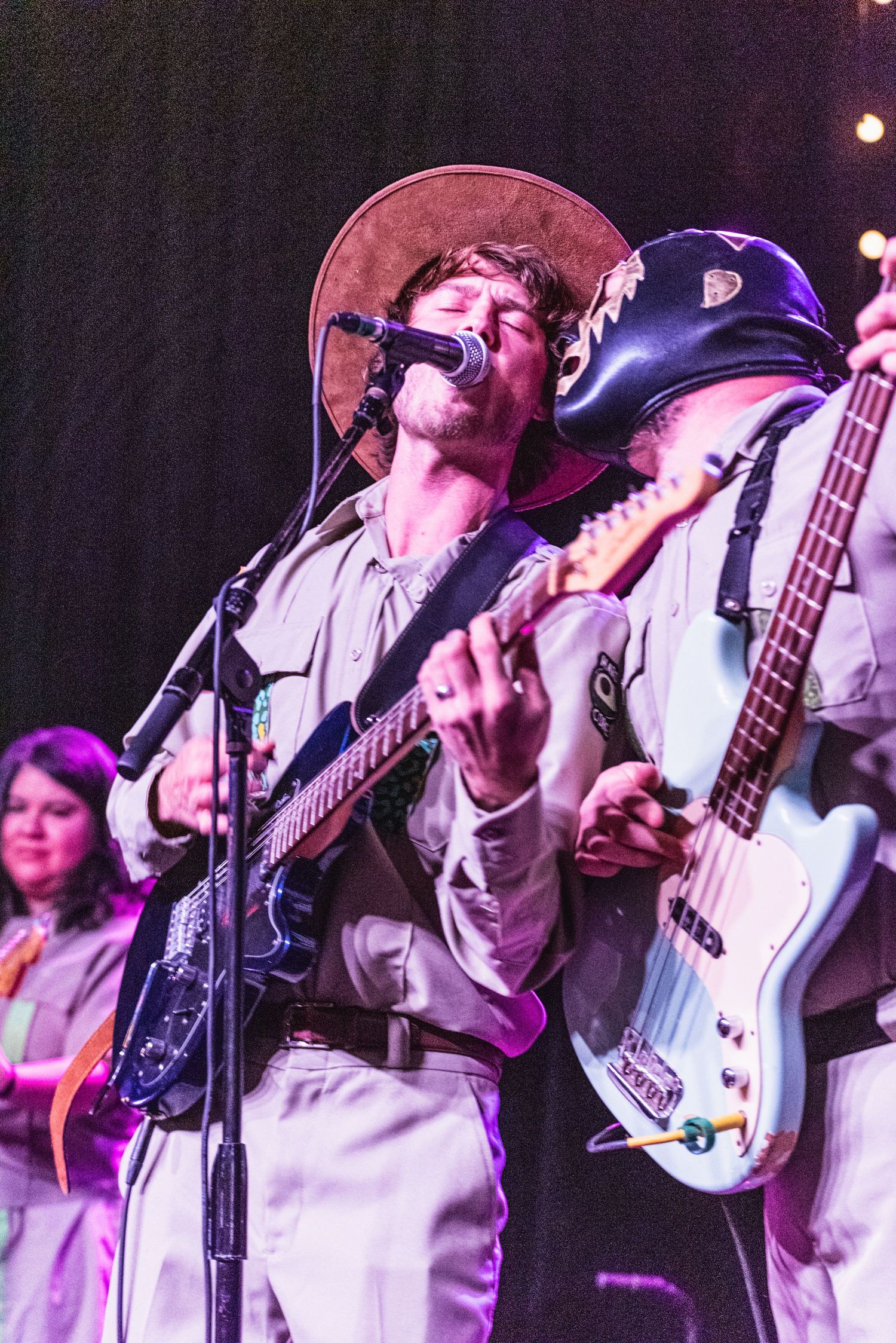 Musicians perform energetically on stage with one singing into microphone while playing blue guitar.