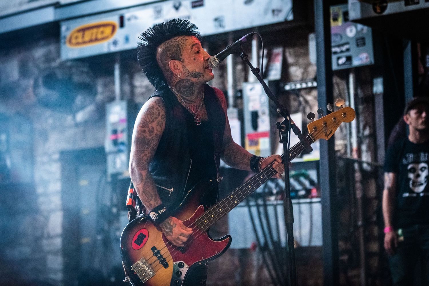 Punk bassist performs with vintage-style bass guitar in smoky urban venue setting.