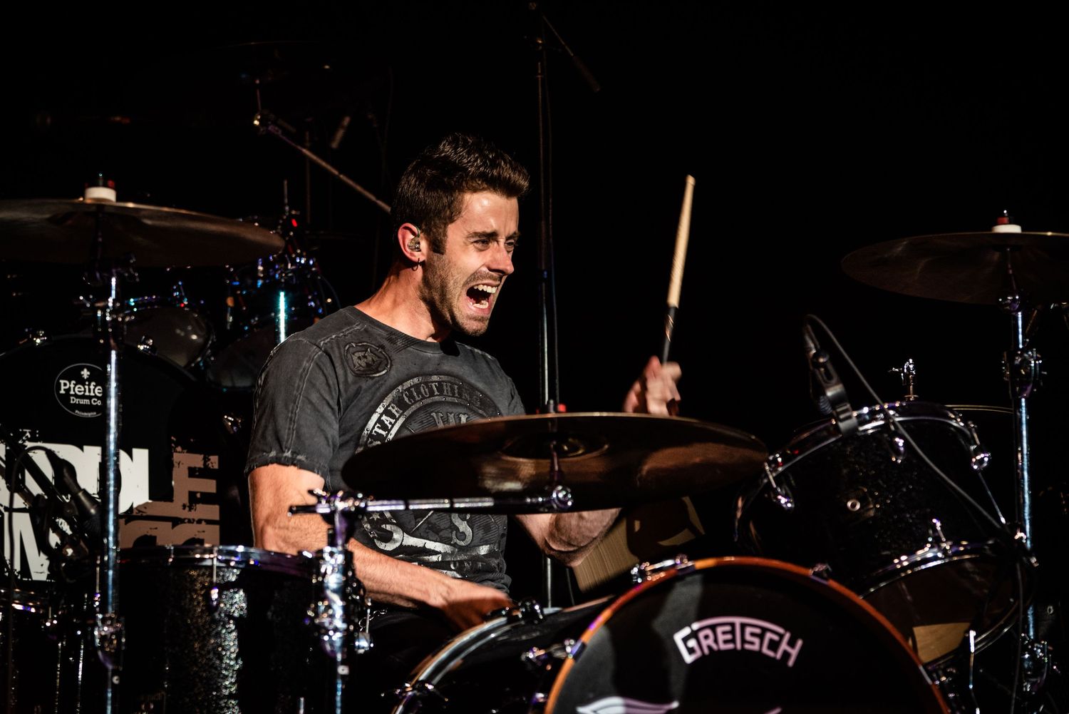 Drummer performing energetically behind drum kit during live concert.