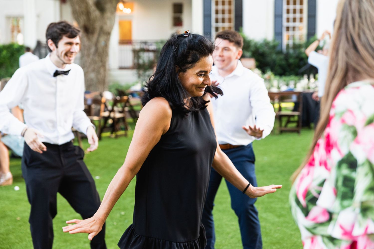 Wedding guests dancing and laughing on a green lawn during an outdoor celebration.