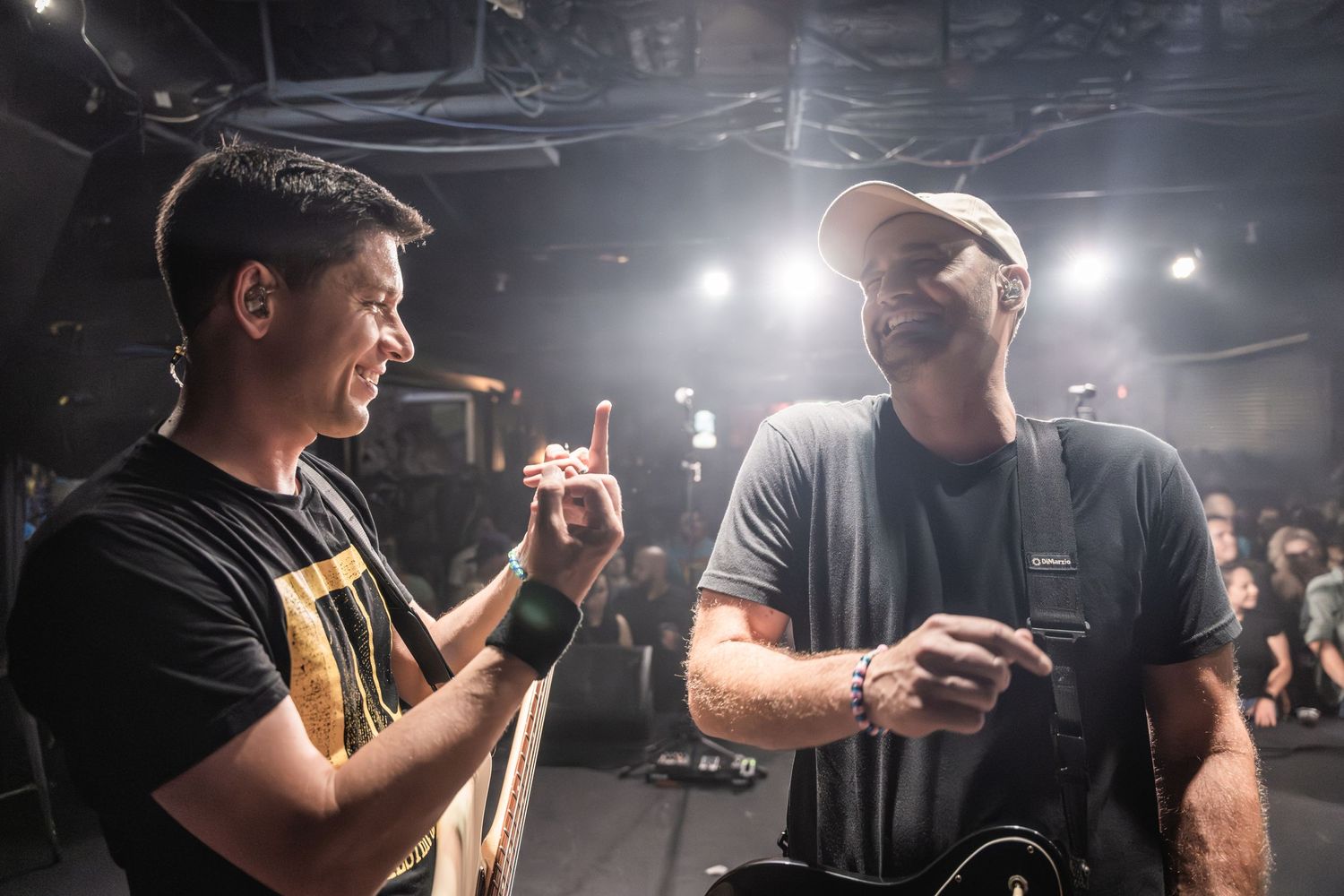 Two musicians share a moment backstage under bright lighting.