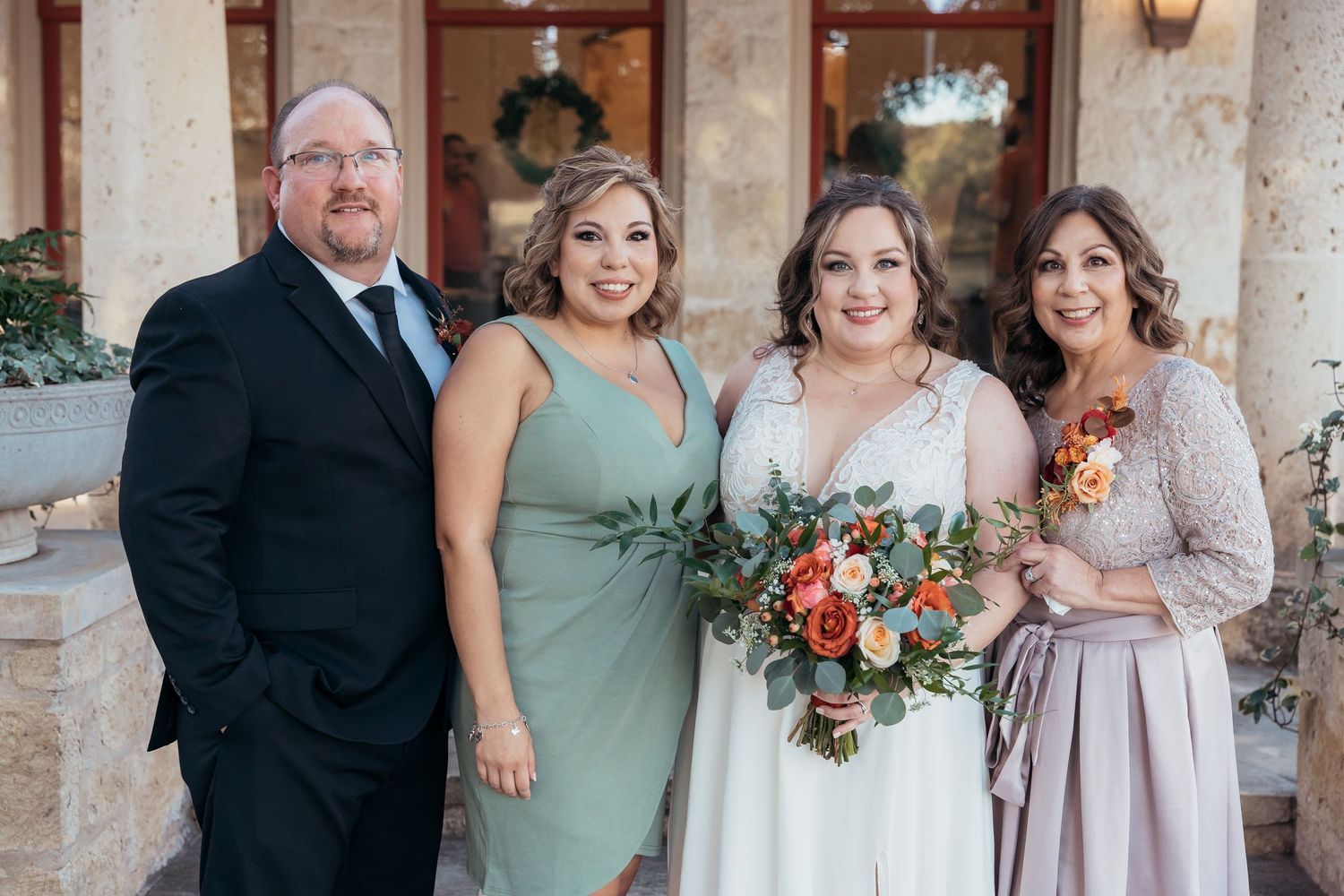 Wedding party poses in coordinated formal attire with peach and green color scheme.