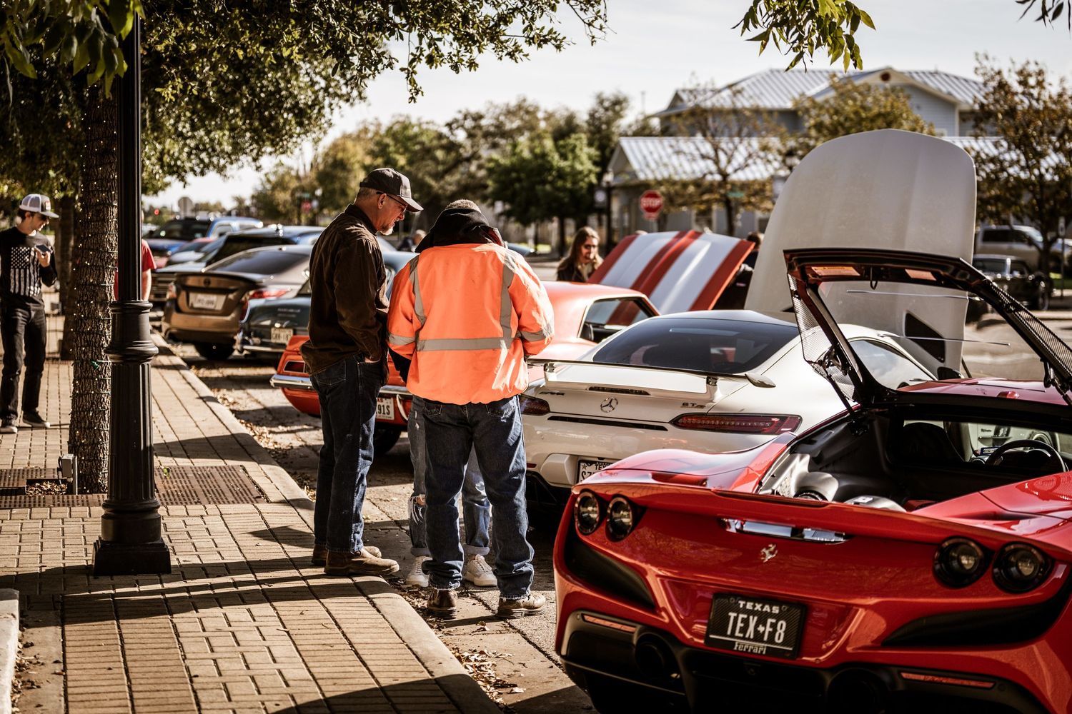 Red sports cars on display at an outdoor car show with spectators viewing engines.