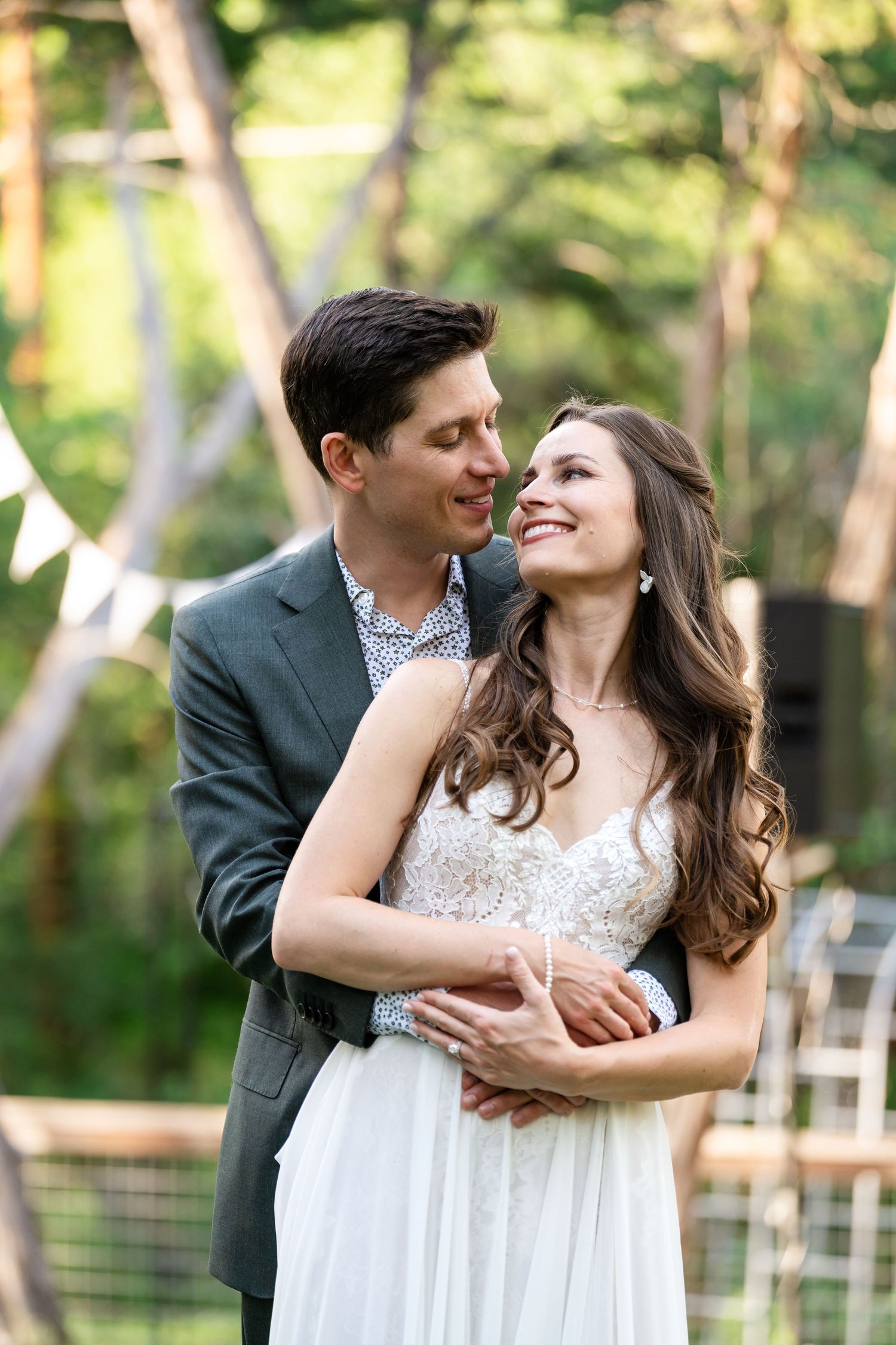 A couple sits together at an outdoor patio table with greenery in the background.