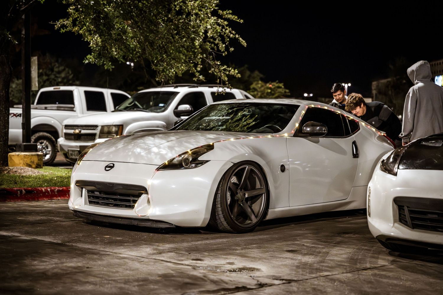 Modified white Nissan 370Z with custom wheels and lowered suspension at a car meet.