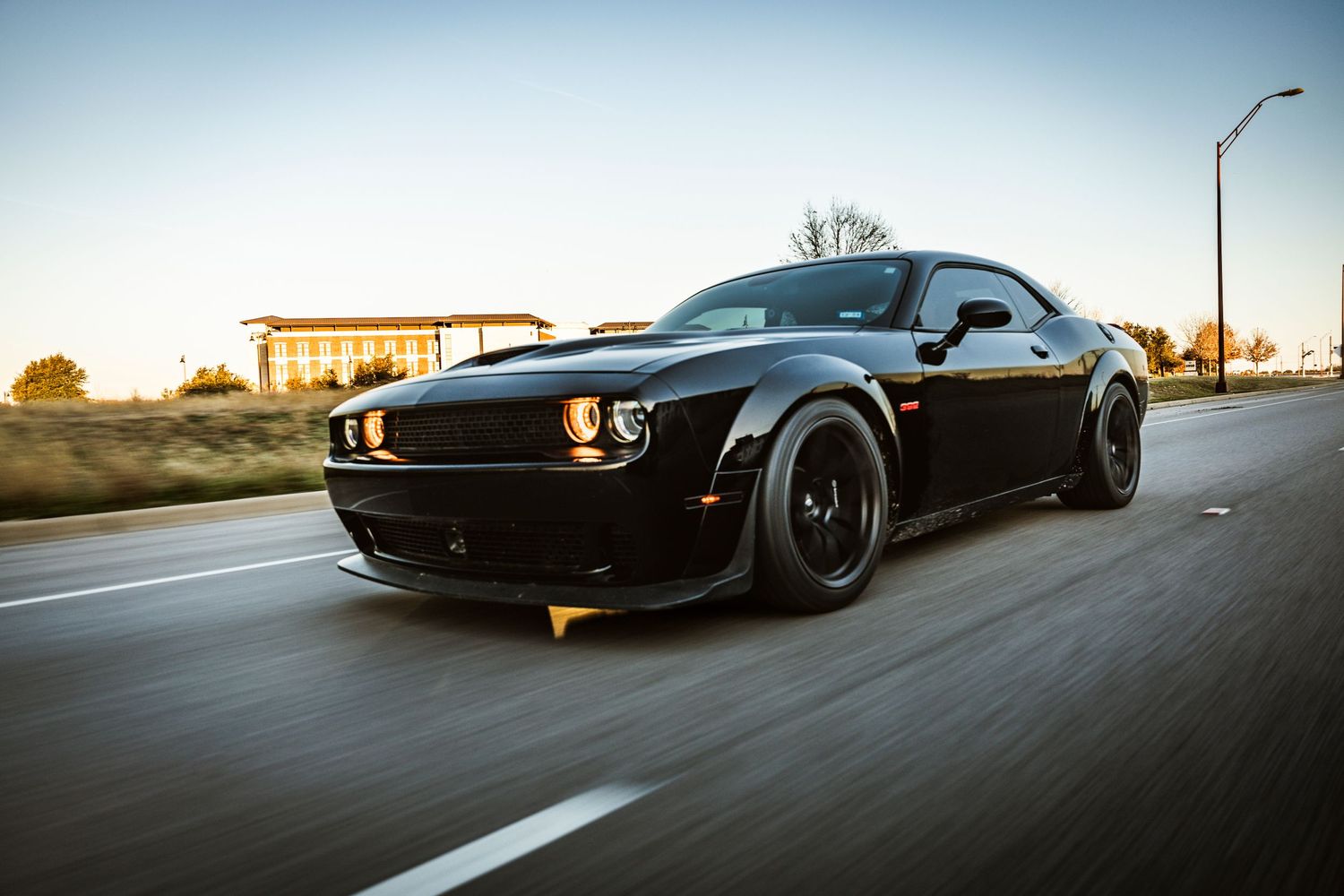 Black Dodge Challenger with custom wheels driving at speed during sunset.