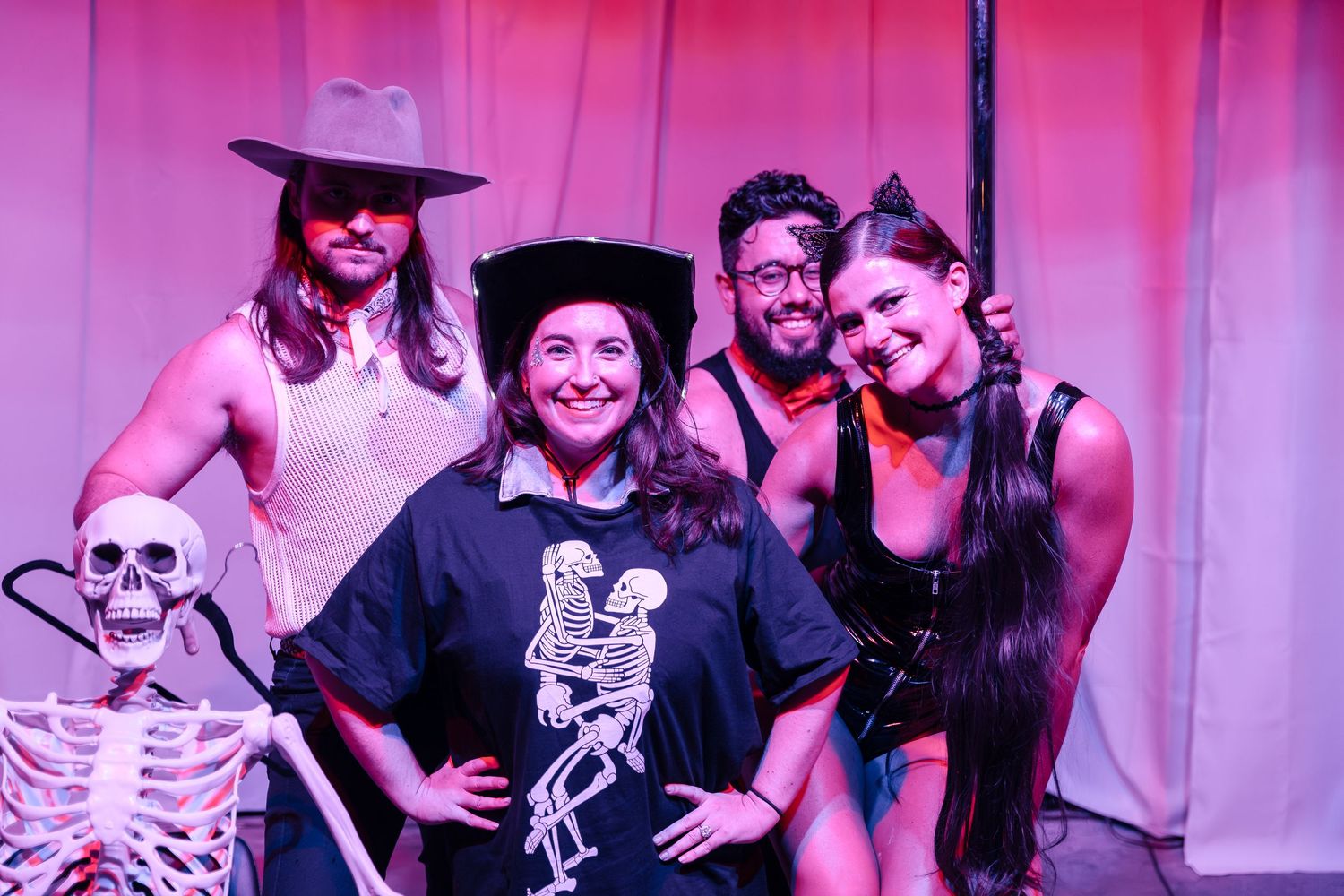Group posing with decorative skeleton prop against pink backdrop at event.