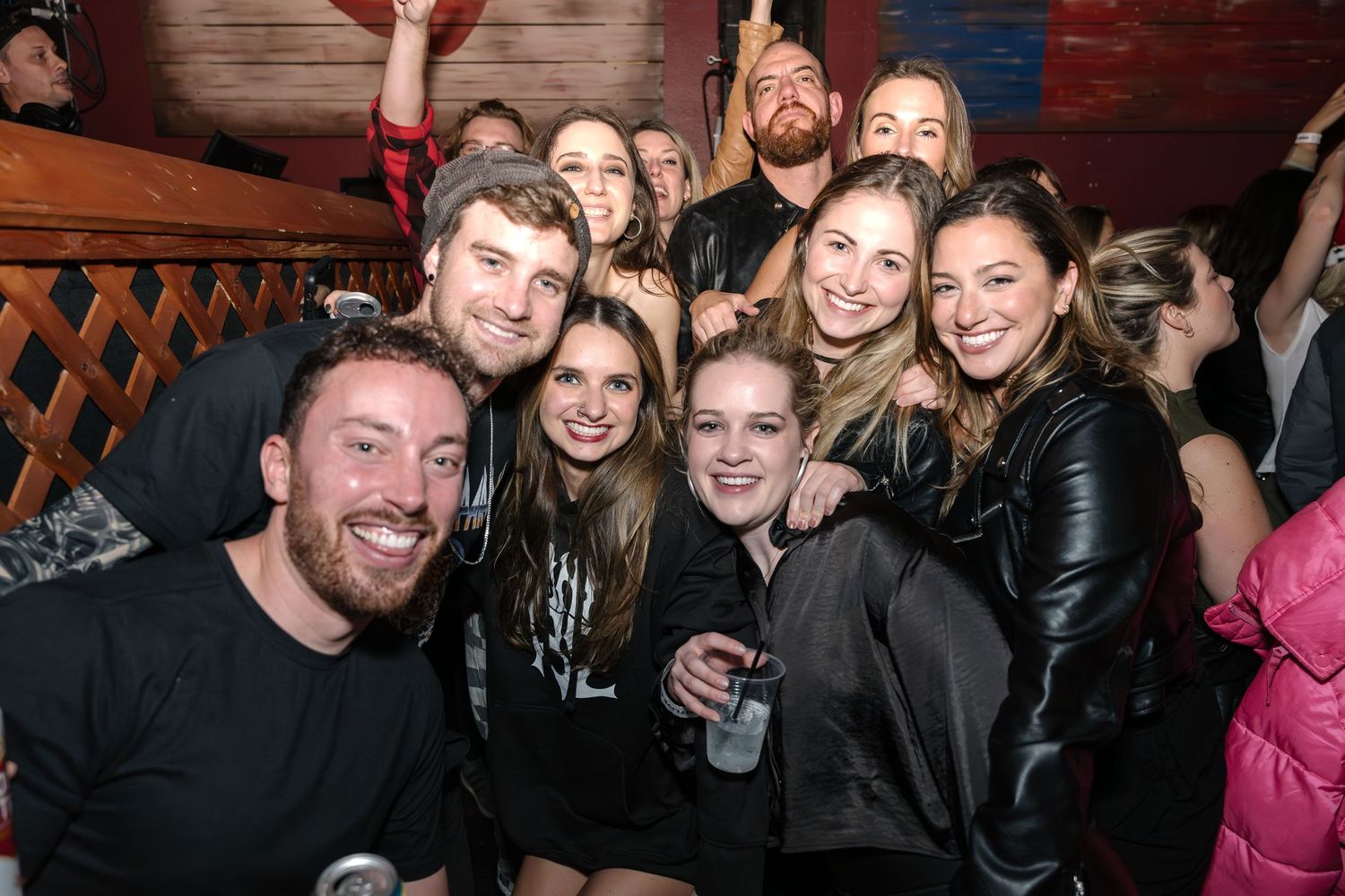 Group of concertgoers posing together for a photo at a music venue with flag decor.