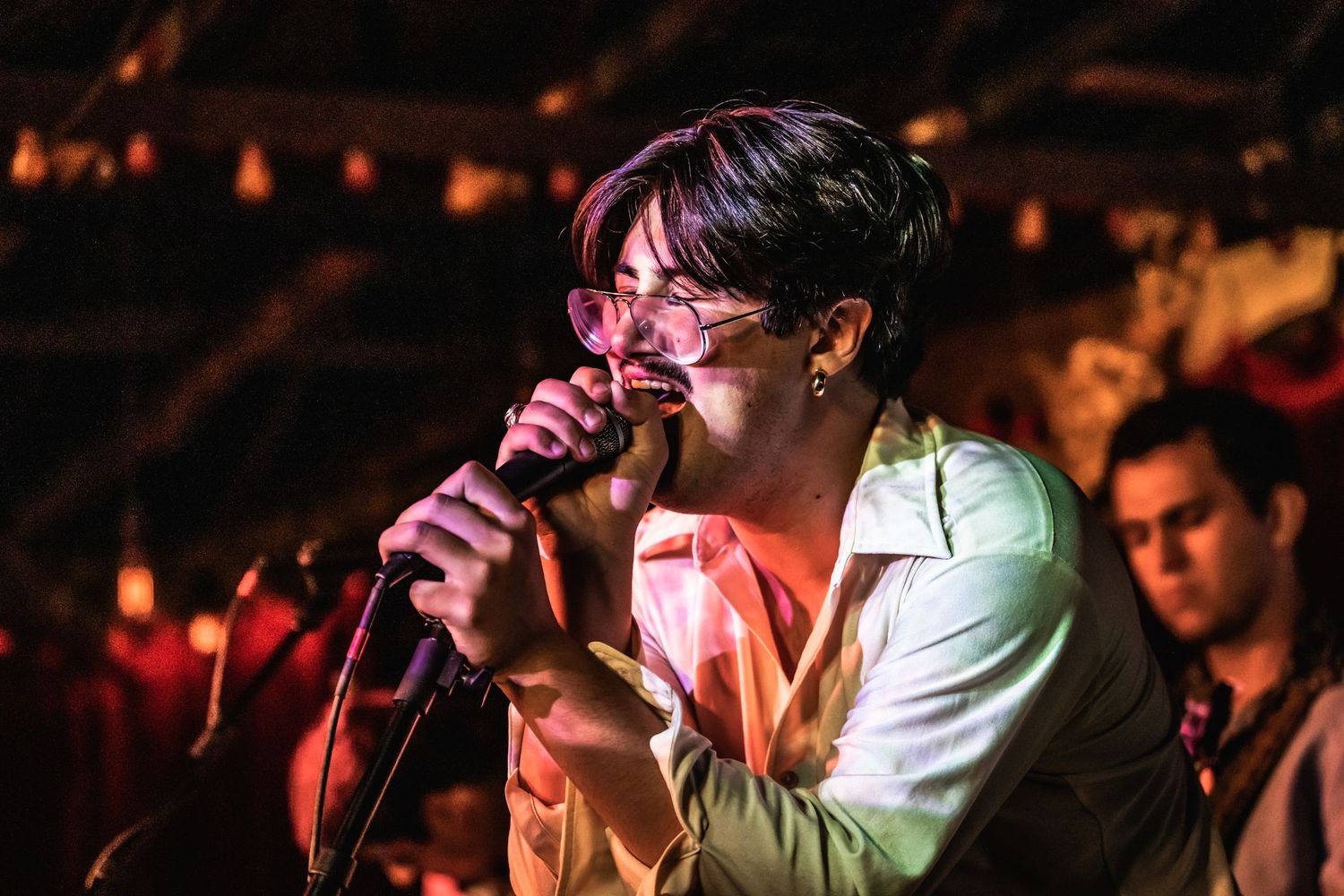 Singer passionately performs on stage with pink lighting and crowd in background.