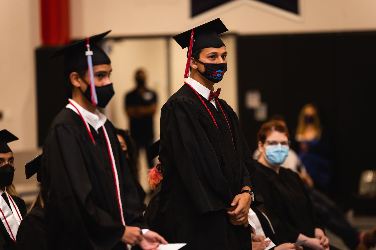 Graduates in black robes and red stoles standing during commencement ceremony.