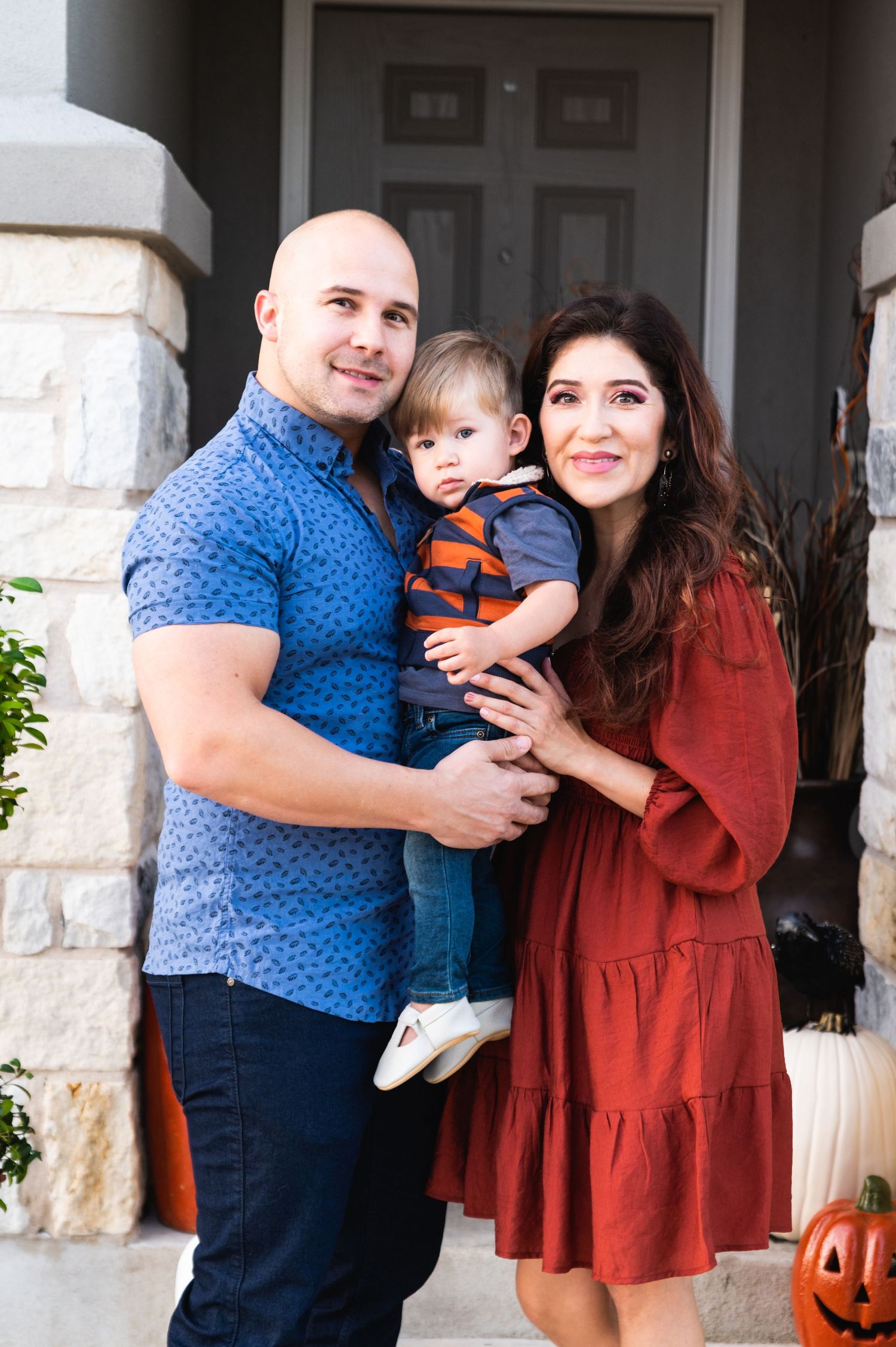 Autumn family portrait on front porch with stone columns and pumpkin decorations.