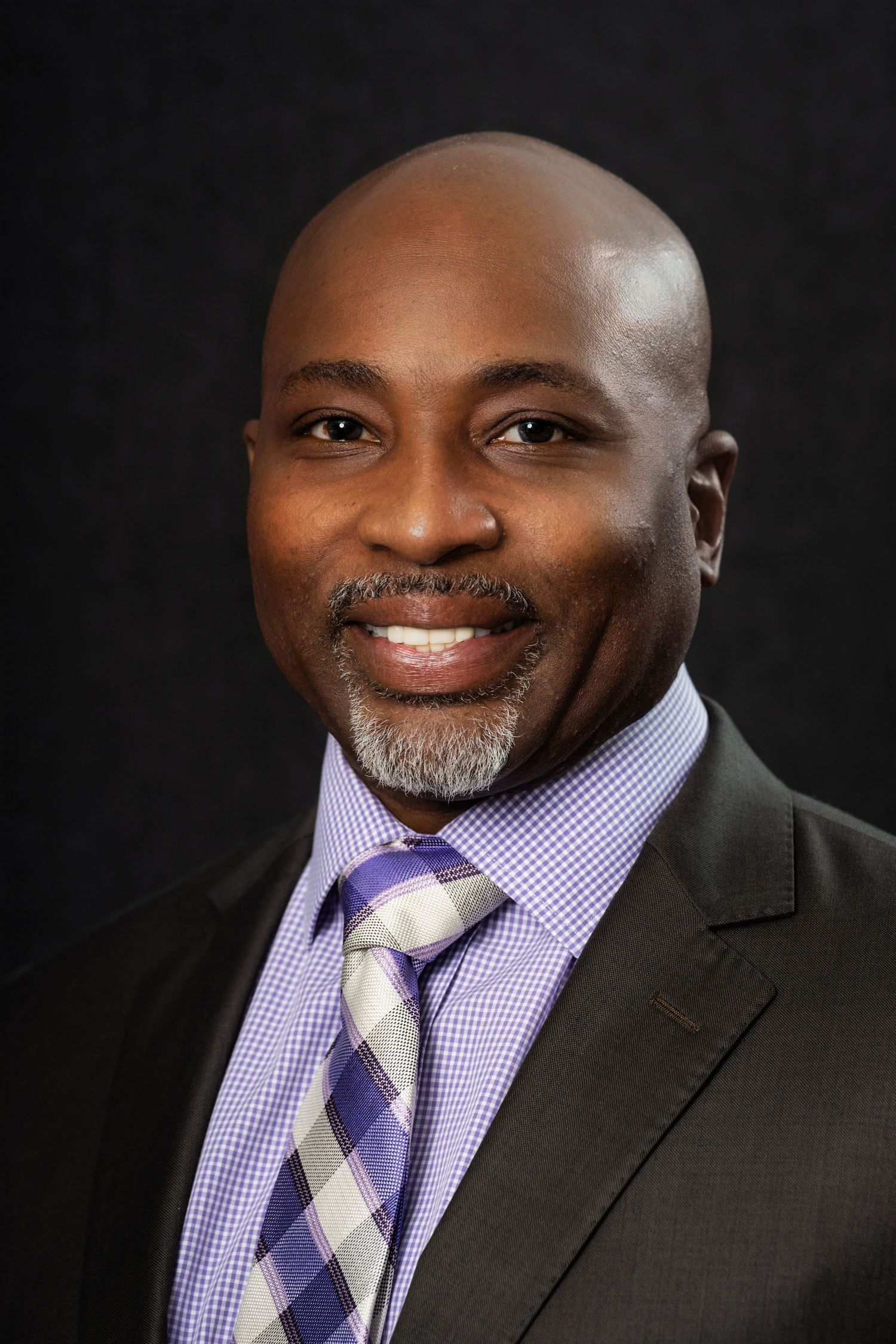 Professional portrait of a person in a purple checkered tie and dark suit jacket.
