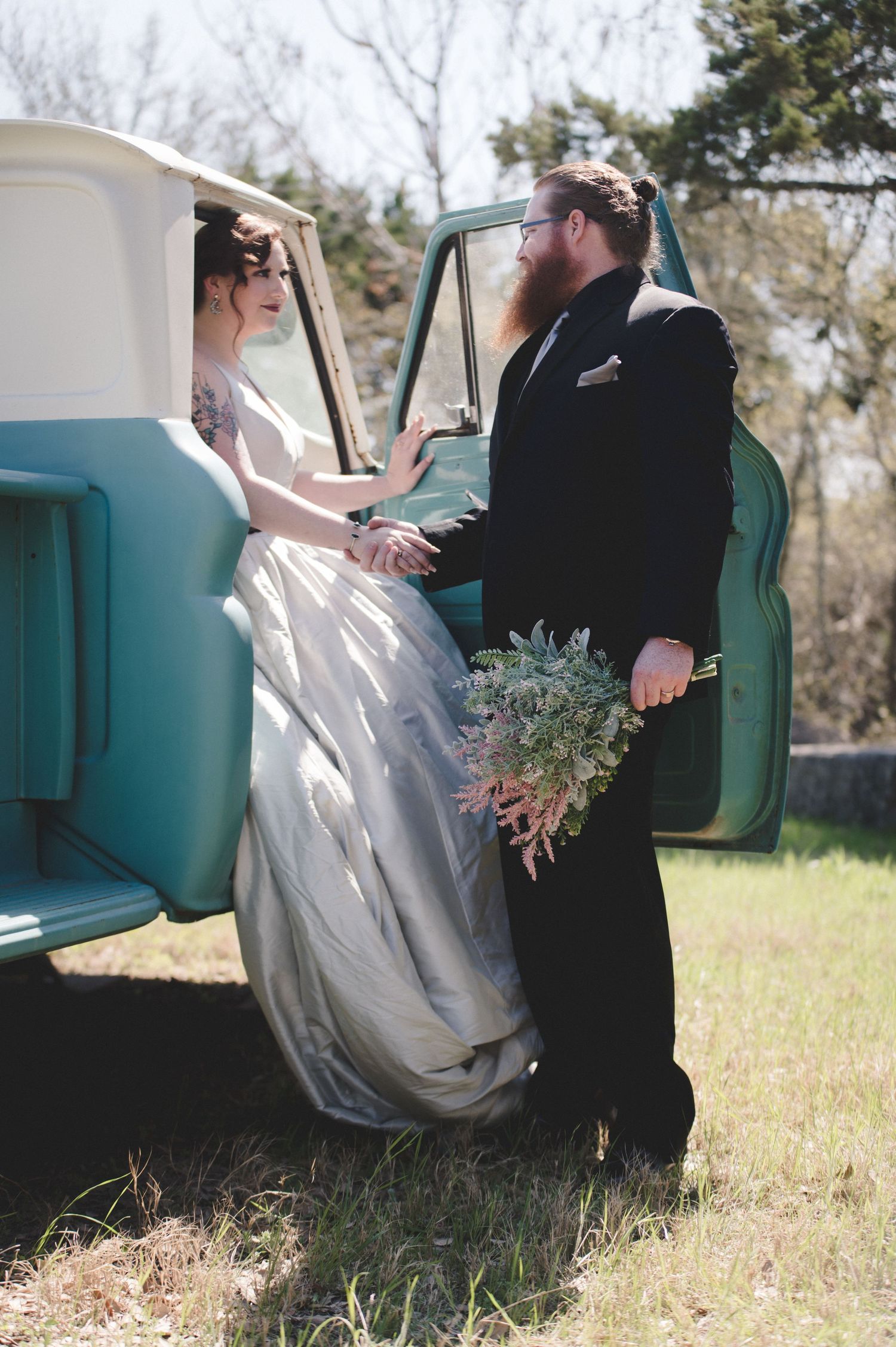 Newlyweds share an intimate moment beside a classic turquoise pickup truck.