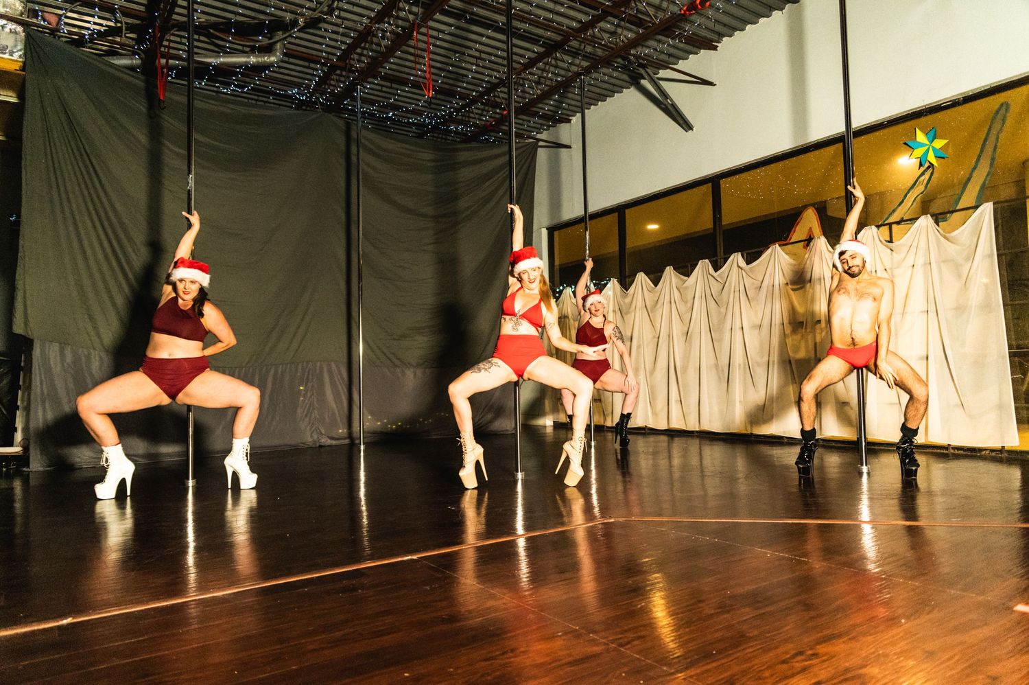 Dancers in red costumes performing synchronized pole dance routine on illuminated stage.