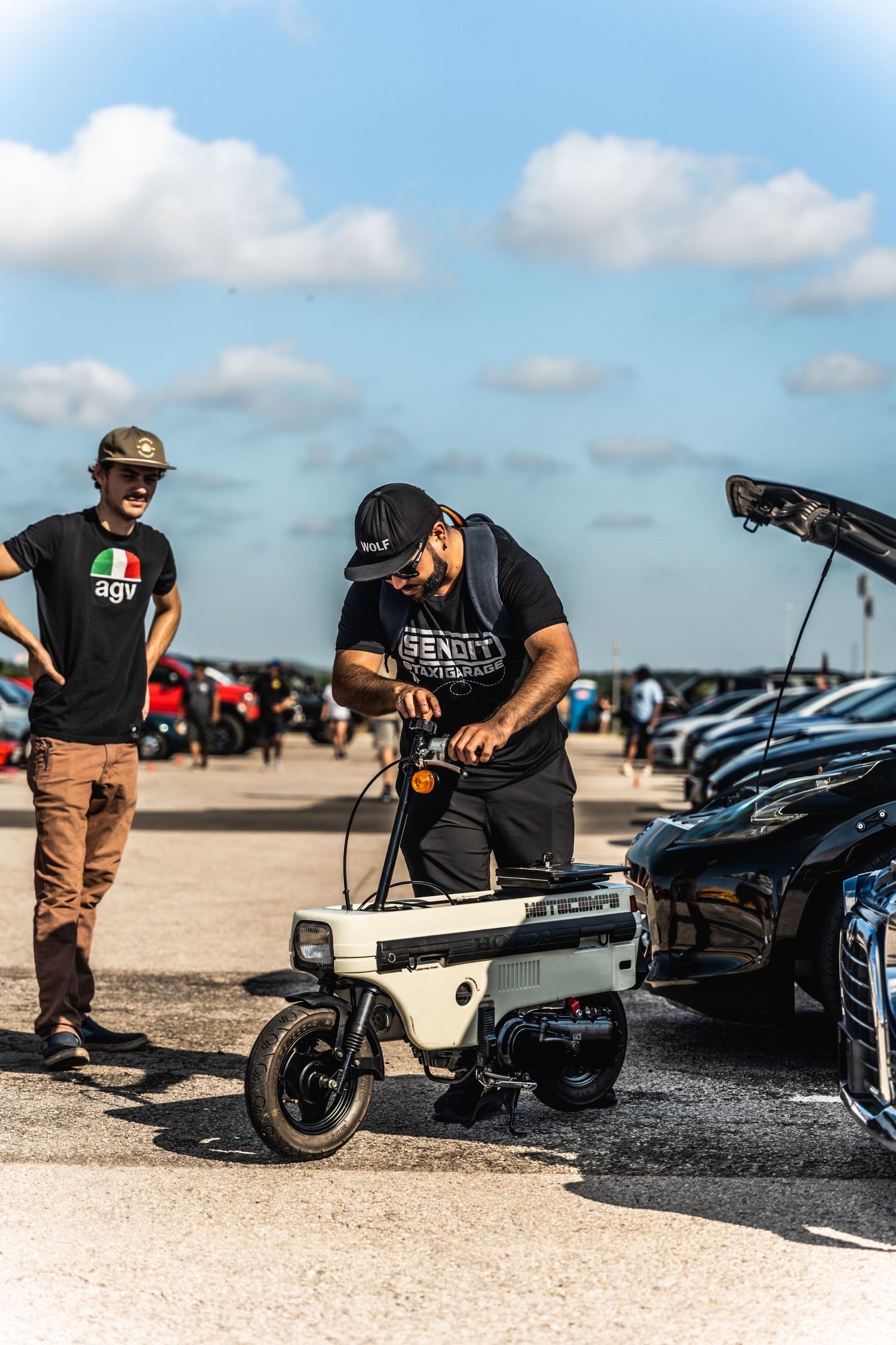 People working with audio equipment at a car show on a sunny day.