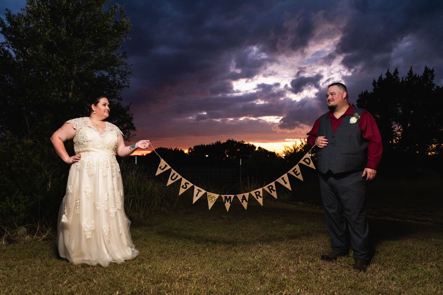 A couple poses with decorative bunting during sunset with dramatic storm clouds in the background.