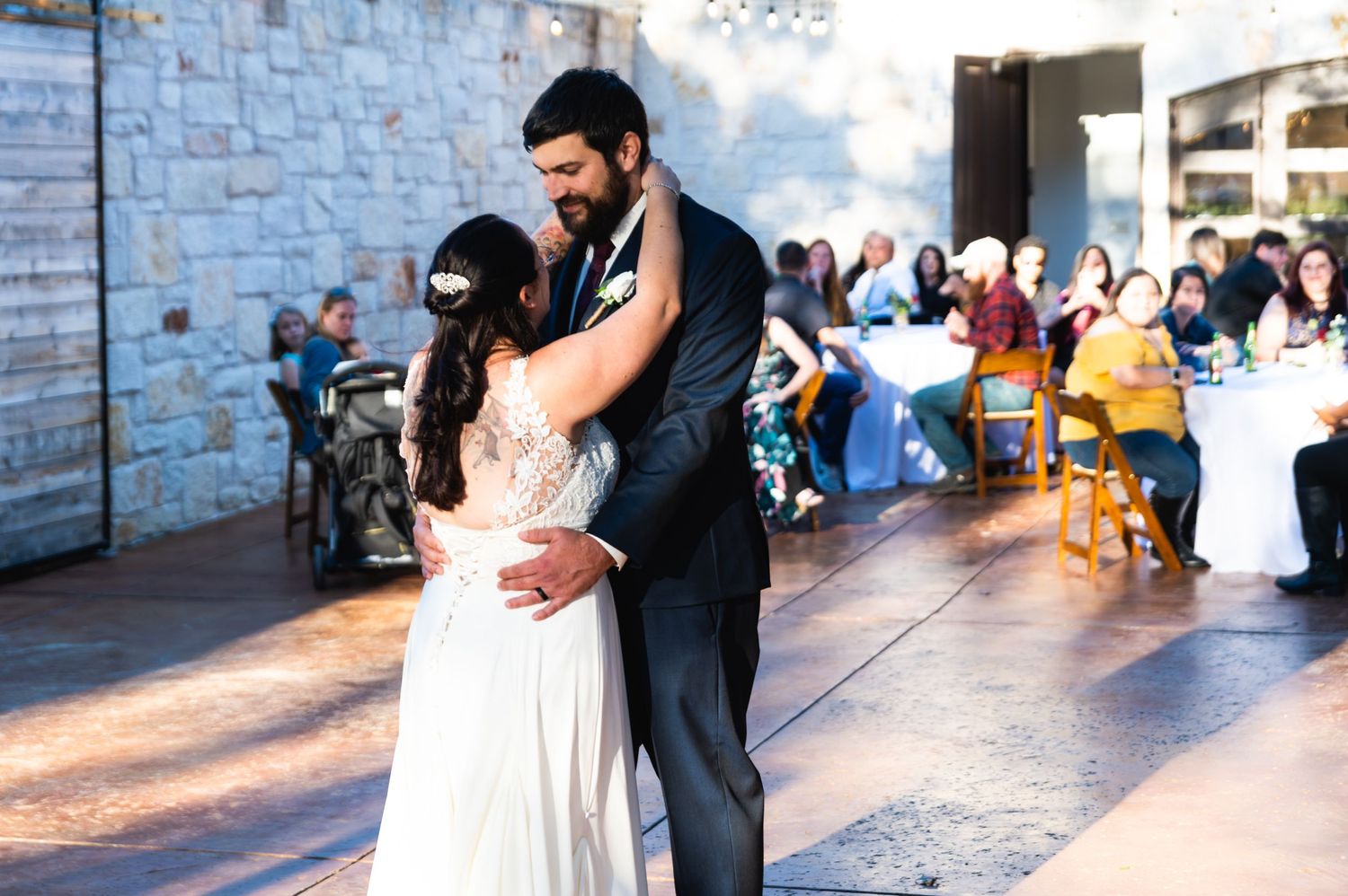 A couple shares their first dance at an outdoor wedding reception with guests watching in the background.