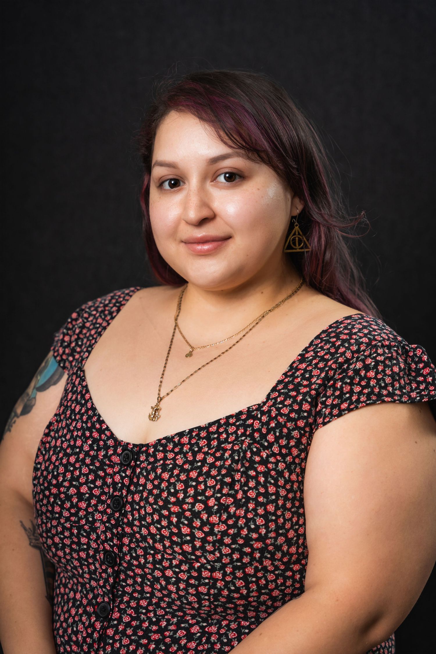 Portrait of smiling person in floral print dress with layered necklaces against dark background.