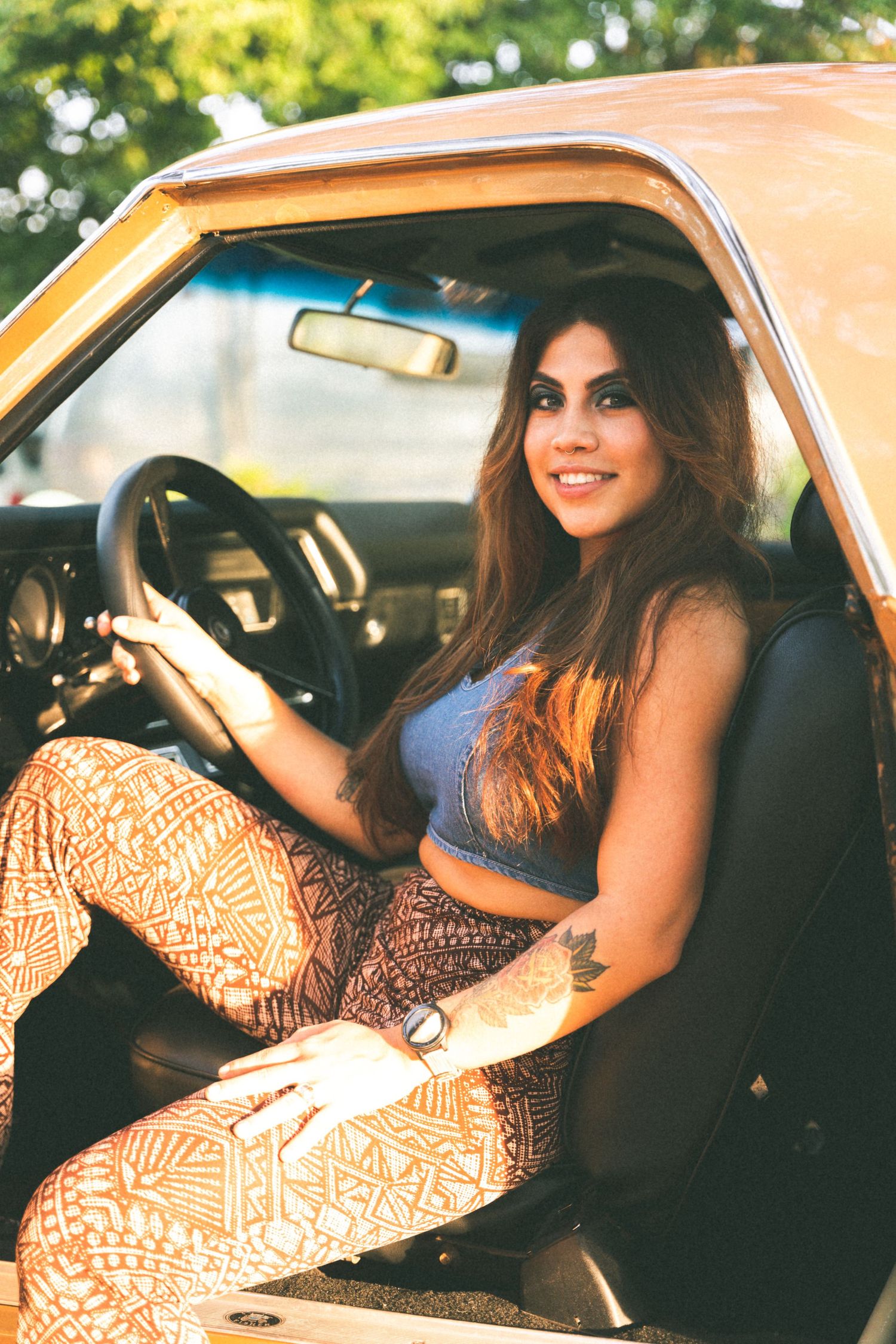 Woman sitting in driver's seat of orange vintage car wearing patterned pants.