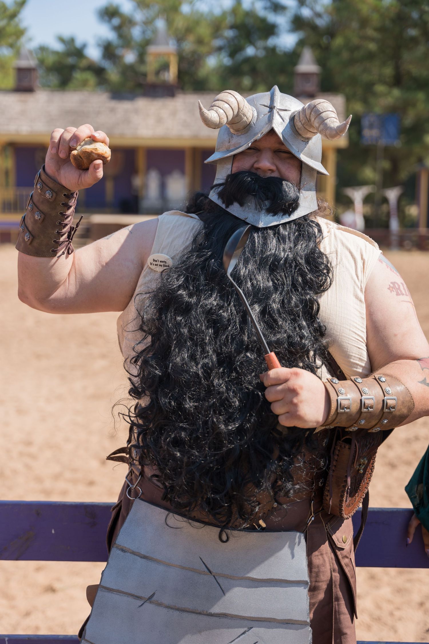 A performer in medieval costume with long dark hair and metal armor gestures dramatically outdoors.