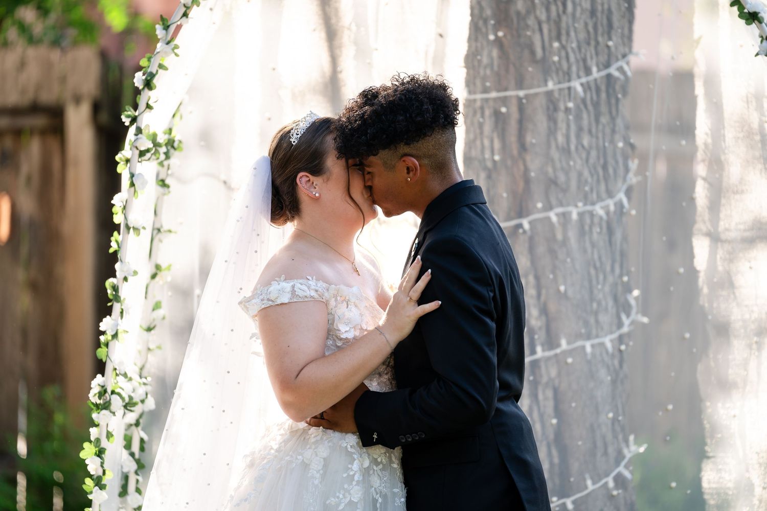 A tender moment between newlyweds sharing an intimate kiss under a decorated wedding arch.