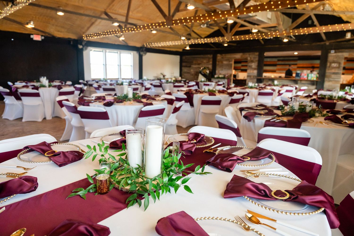 Wedding reception venue with burgundy and white table settings and elegant centerpieces.