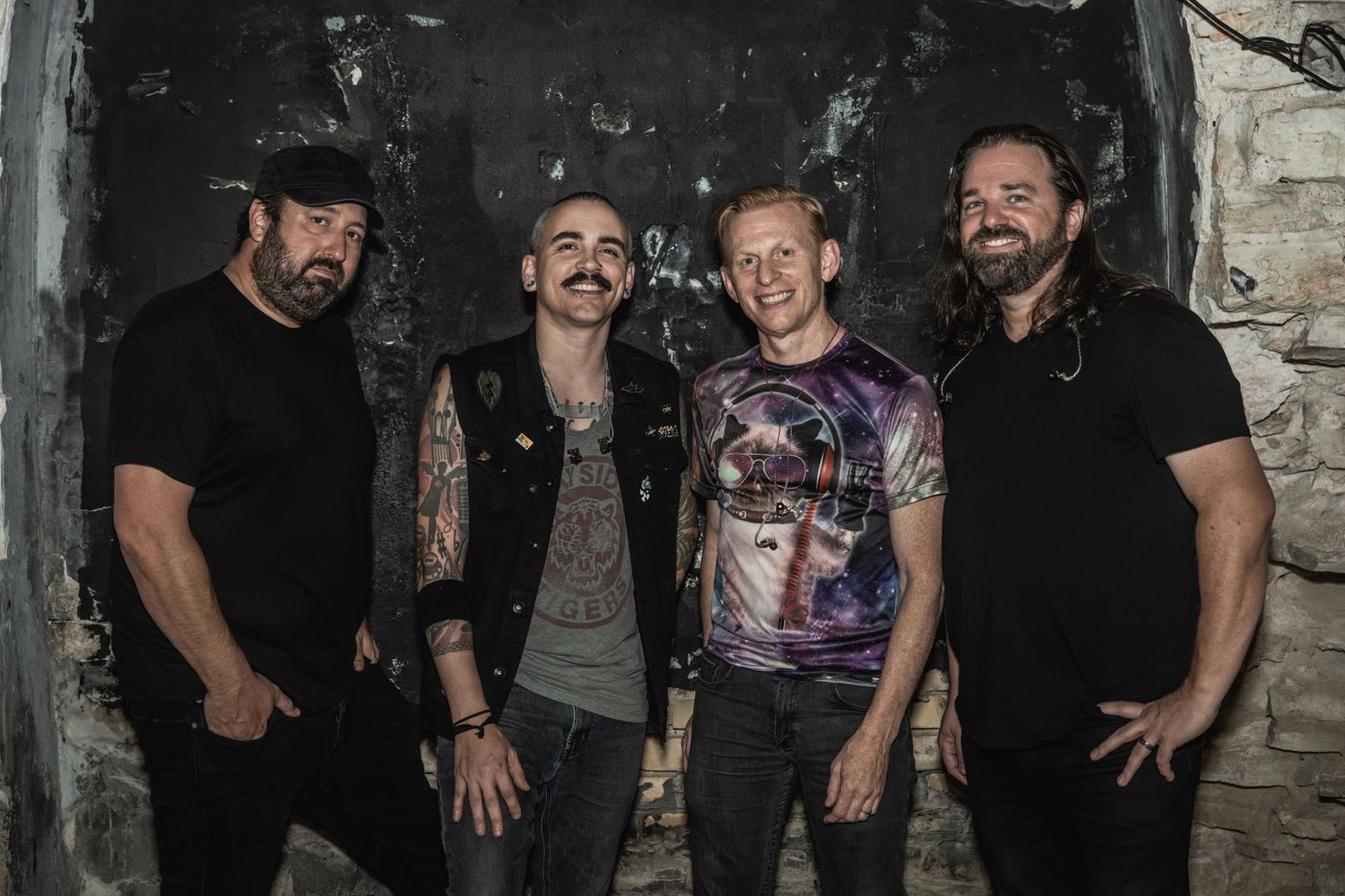 Four musicians pose in dark clothing against a grungy stone wall background.