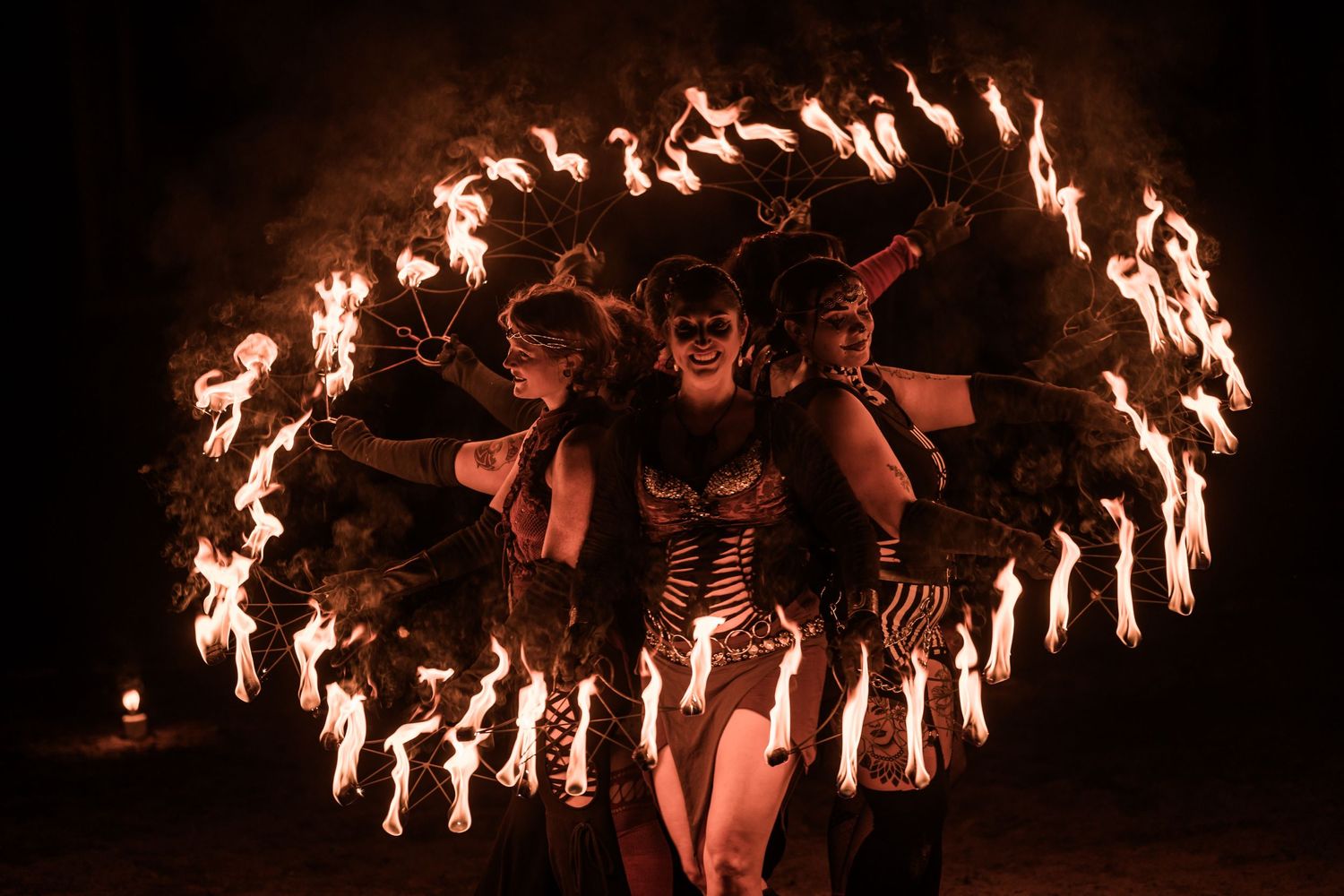 Group fire dance performance creates circular patterns of flames in the darkness.