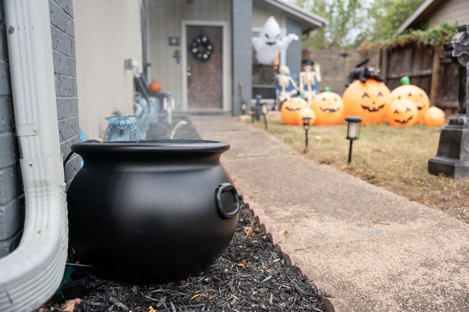 Large black cauldron prop with illuminated Halloween pumpkins decorating a garden pathway.