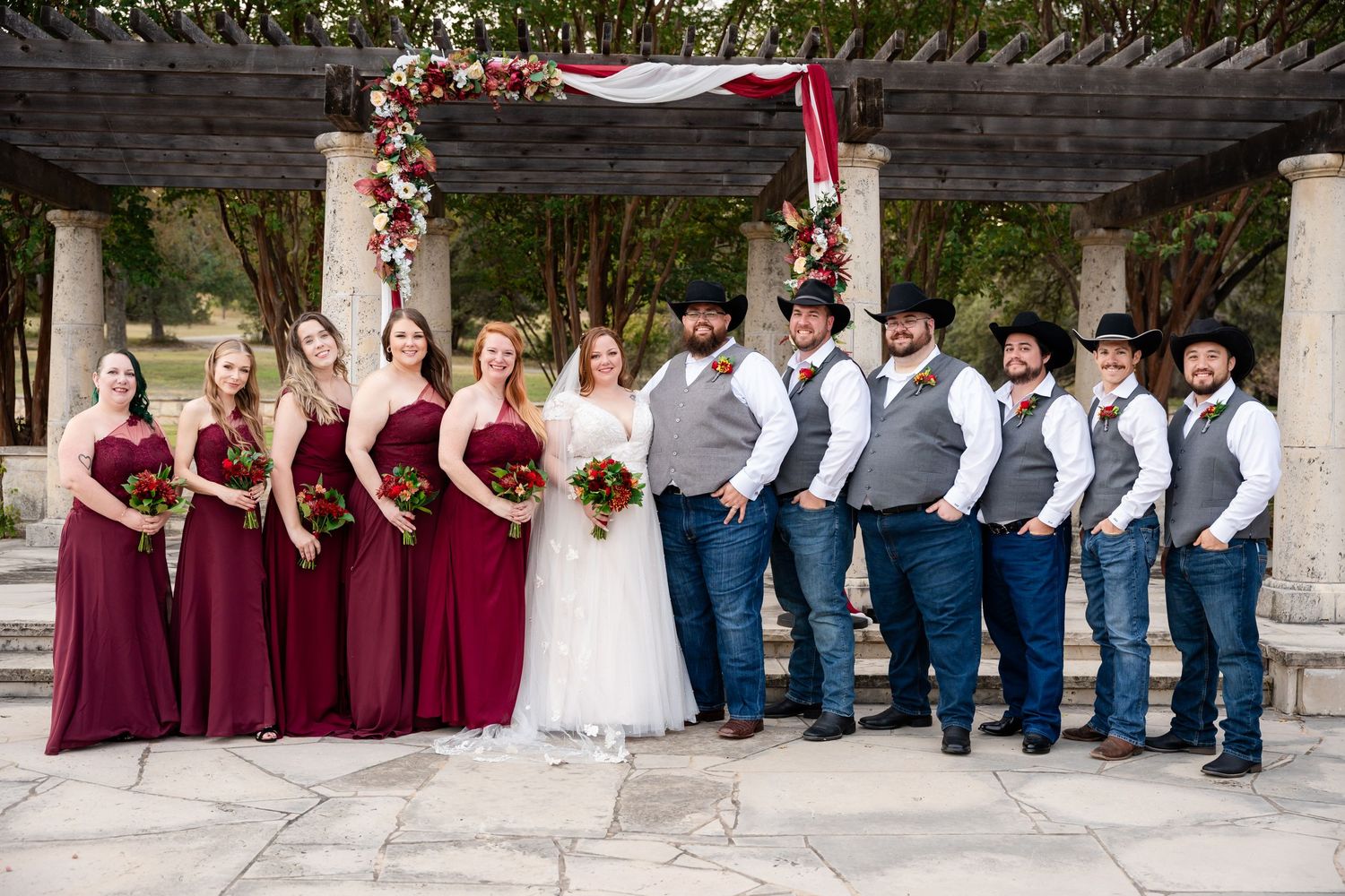 Wedding party lined up under pergola with bridesmaids in burgundy and groomsmen in blue and grey.
