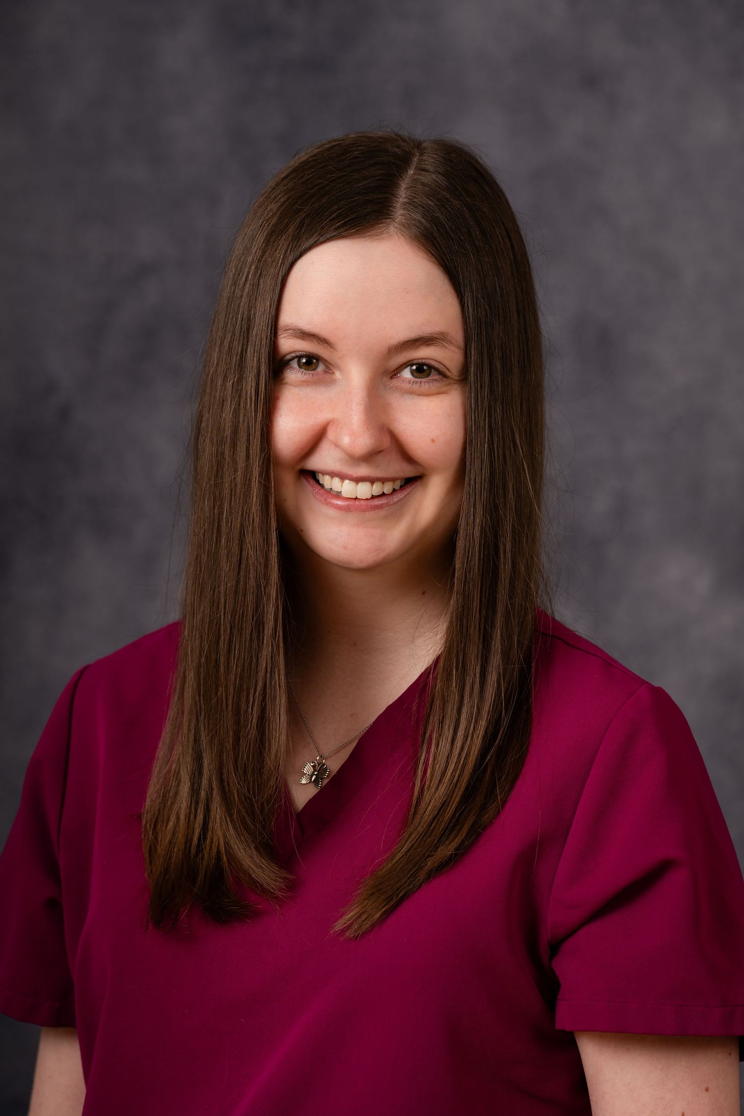 Professional headshot of person in burgundy scrubs against gray backdrop.