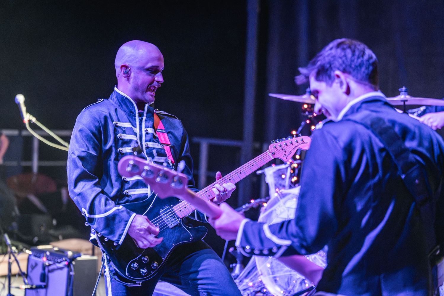Musicians in matching uniforms performing with guitars under blue stage lighting.