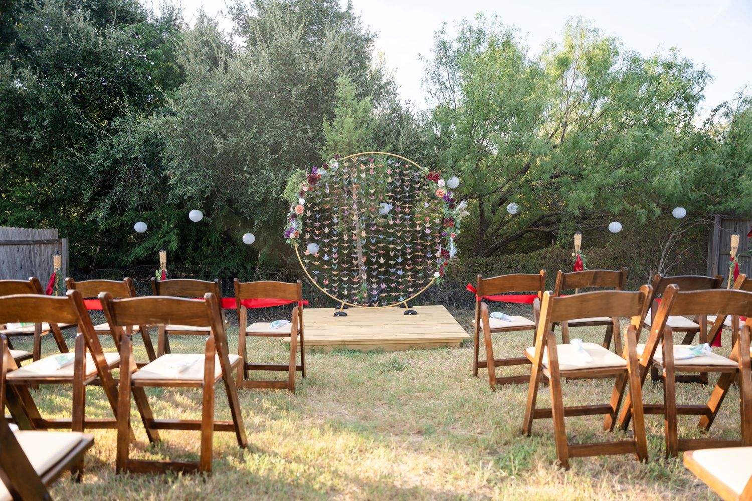 Outdoor wedding ceremony setup with wooden chairs and a decorative floral arch backdrop.