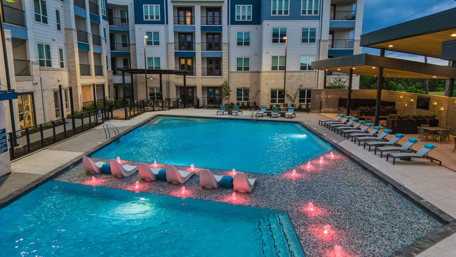 Luxurious apartment pool area with illuminated pink floating loungers and modern architectural design.
