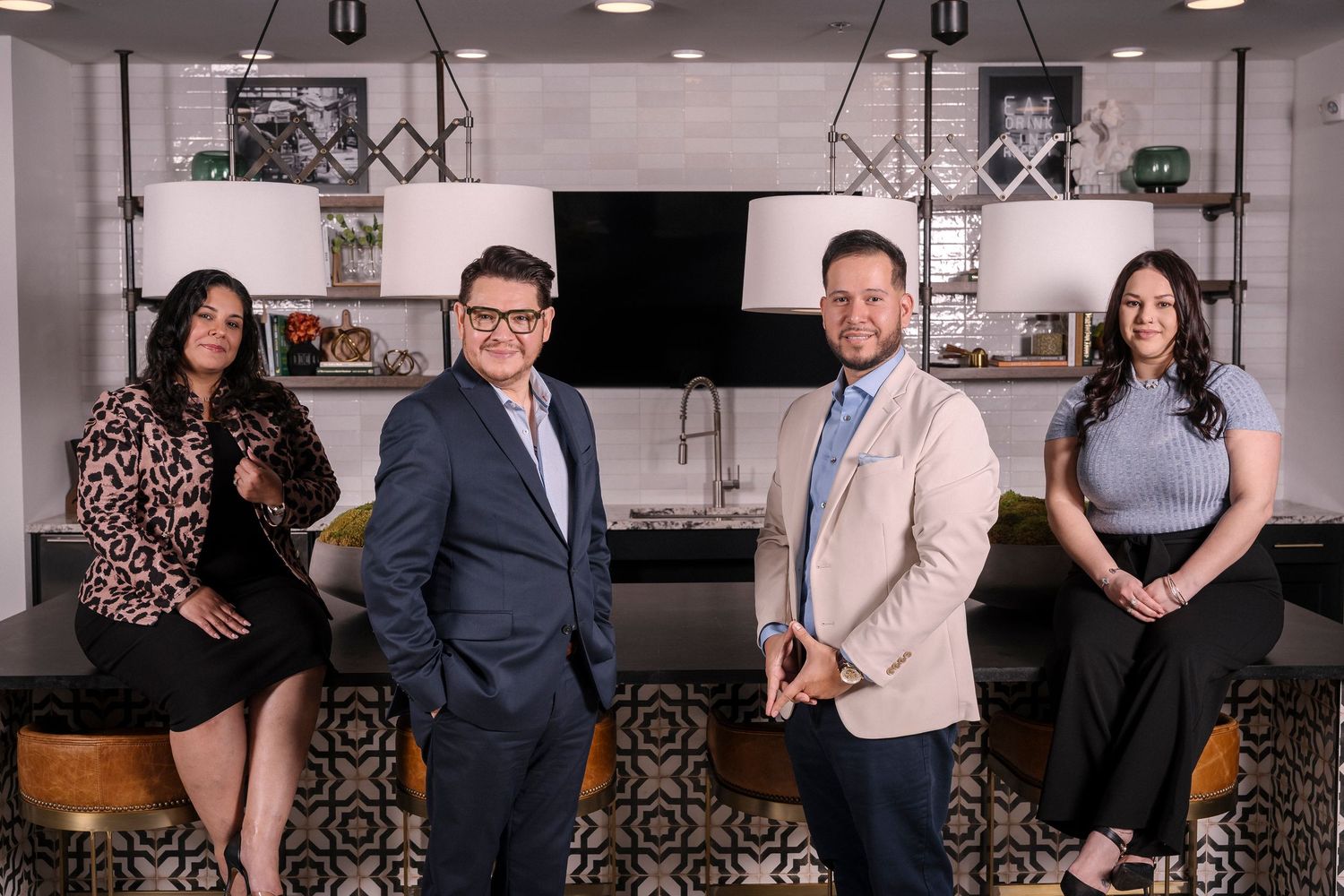 A group of professionally dressed real estate team members pose together in a modern kitchen with stylish decor.