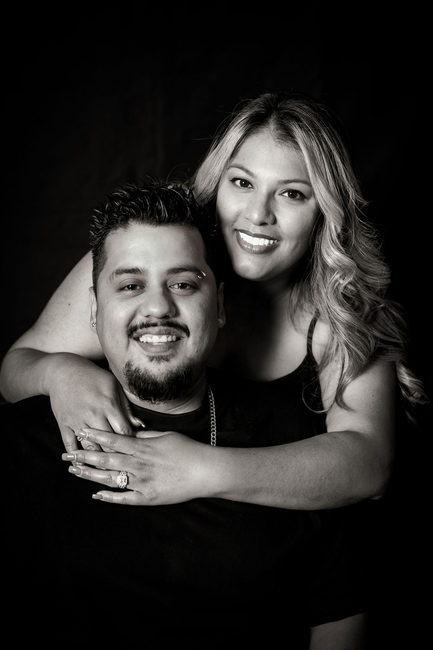 Affectionate black and white couple portrait with genuine smiles against dark background.