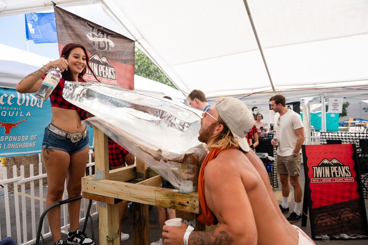 People participating in ice luge drinks at outdoor festival tent.