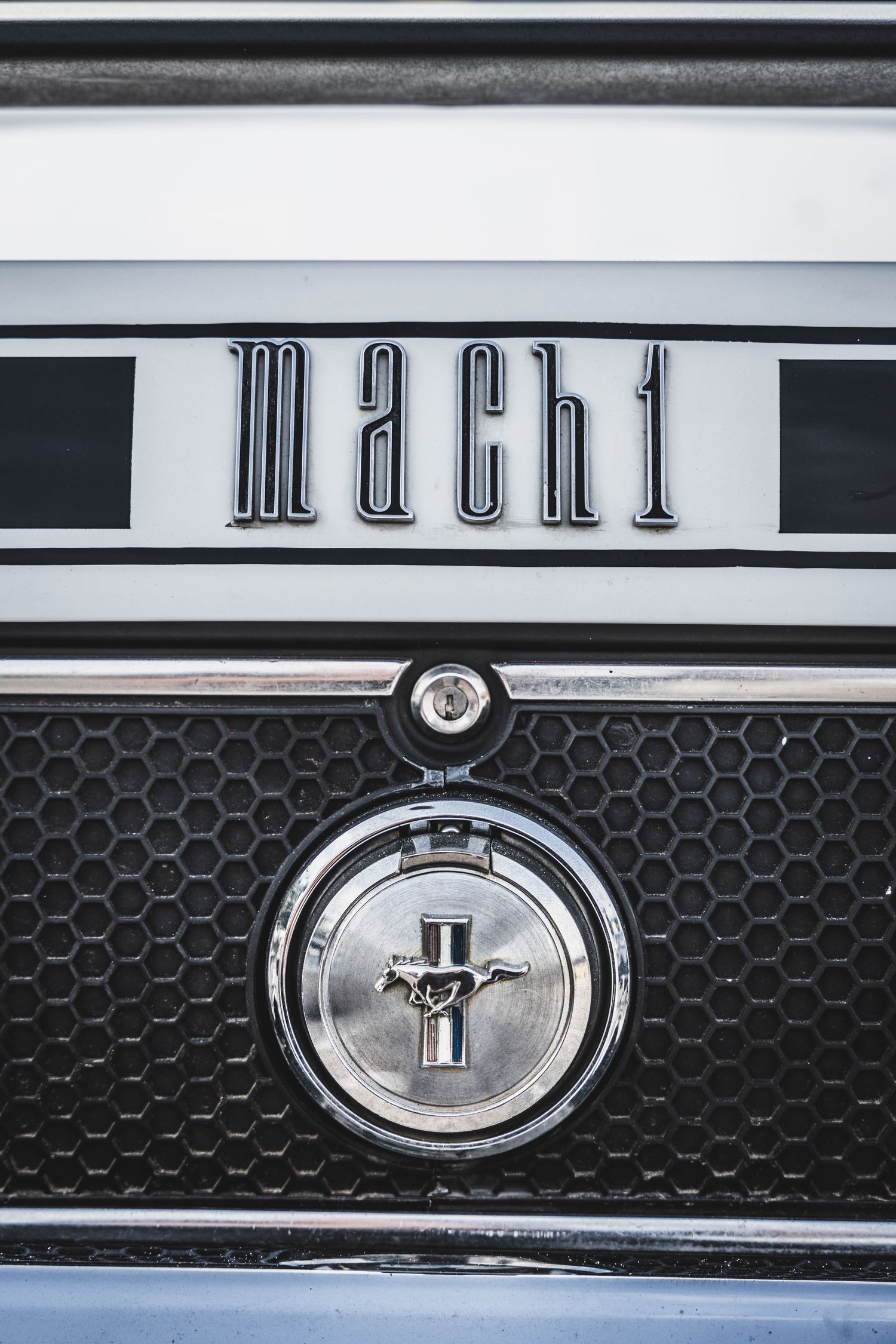 Close-up of vintage Mach 1 badge and Ford Mustang emblem on honeycomb grille.