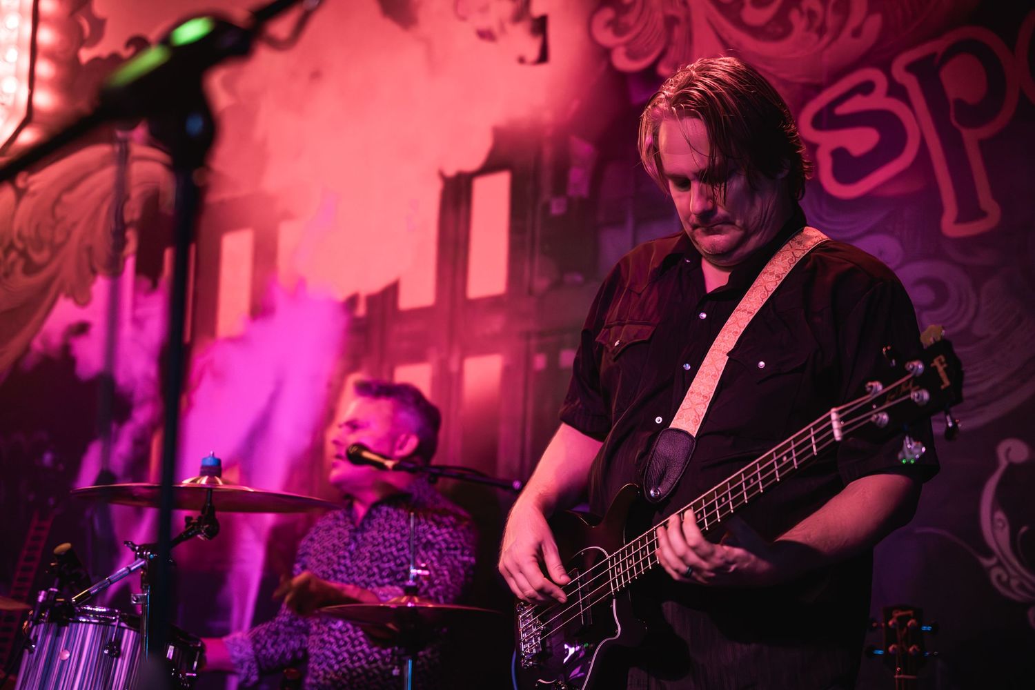 Musicians performing on stage with vibrant pink and purple lighting effects.