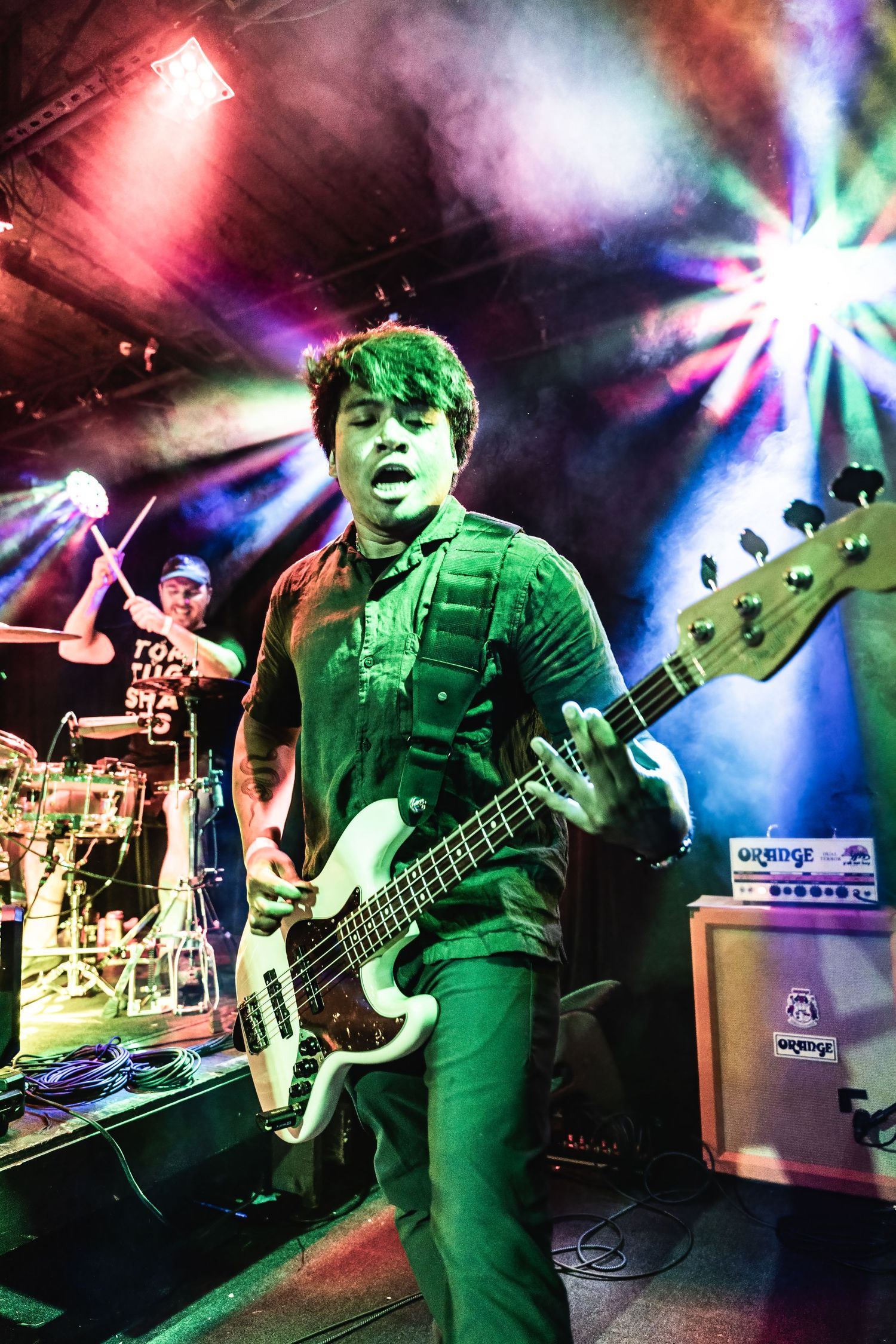 Bassist plays under colorful stage lighting and smoke effects during energetic performance.