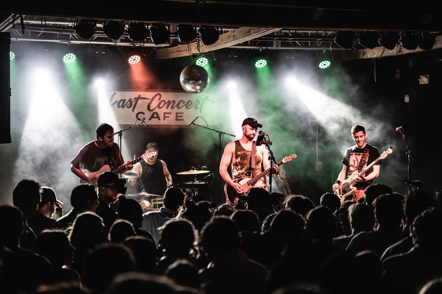 Band performs on stage with dramatic lighting and fog effects while crowd watches in foreground.