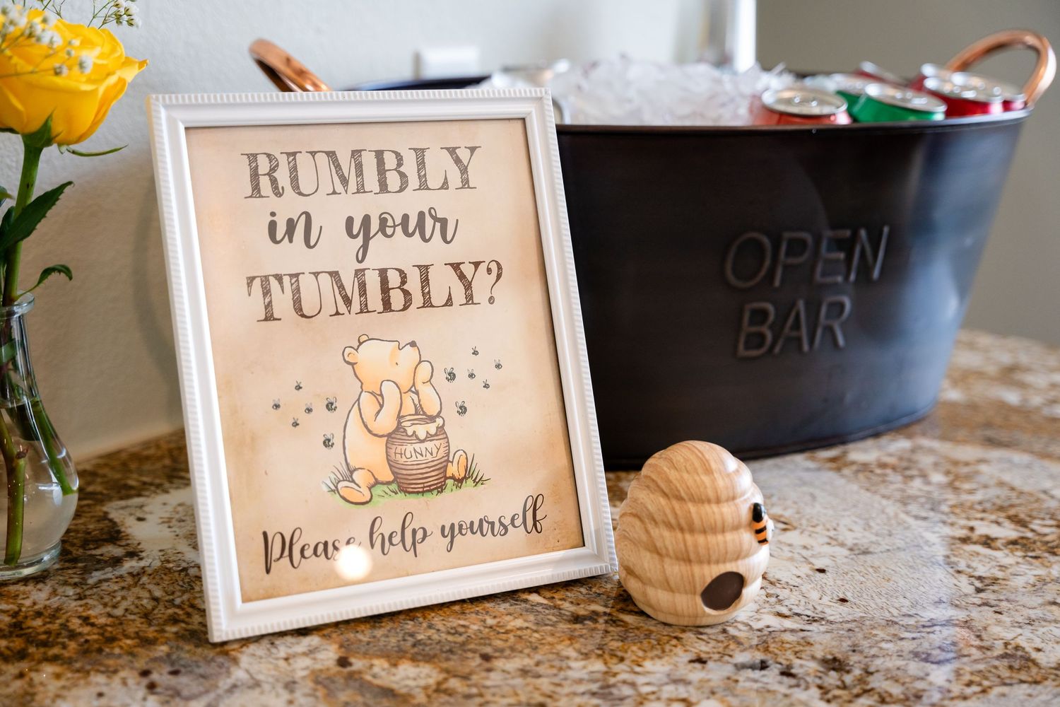 Winnie the Pooh themed party sign reading 'Rumbly in your Tumbly' next to a decorative beehive.