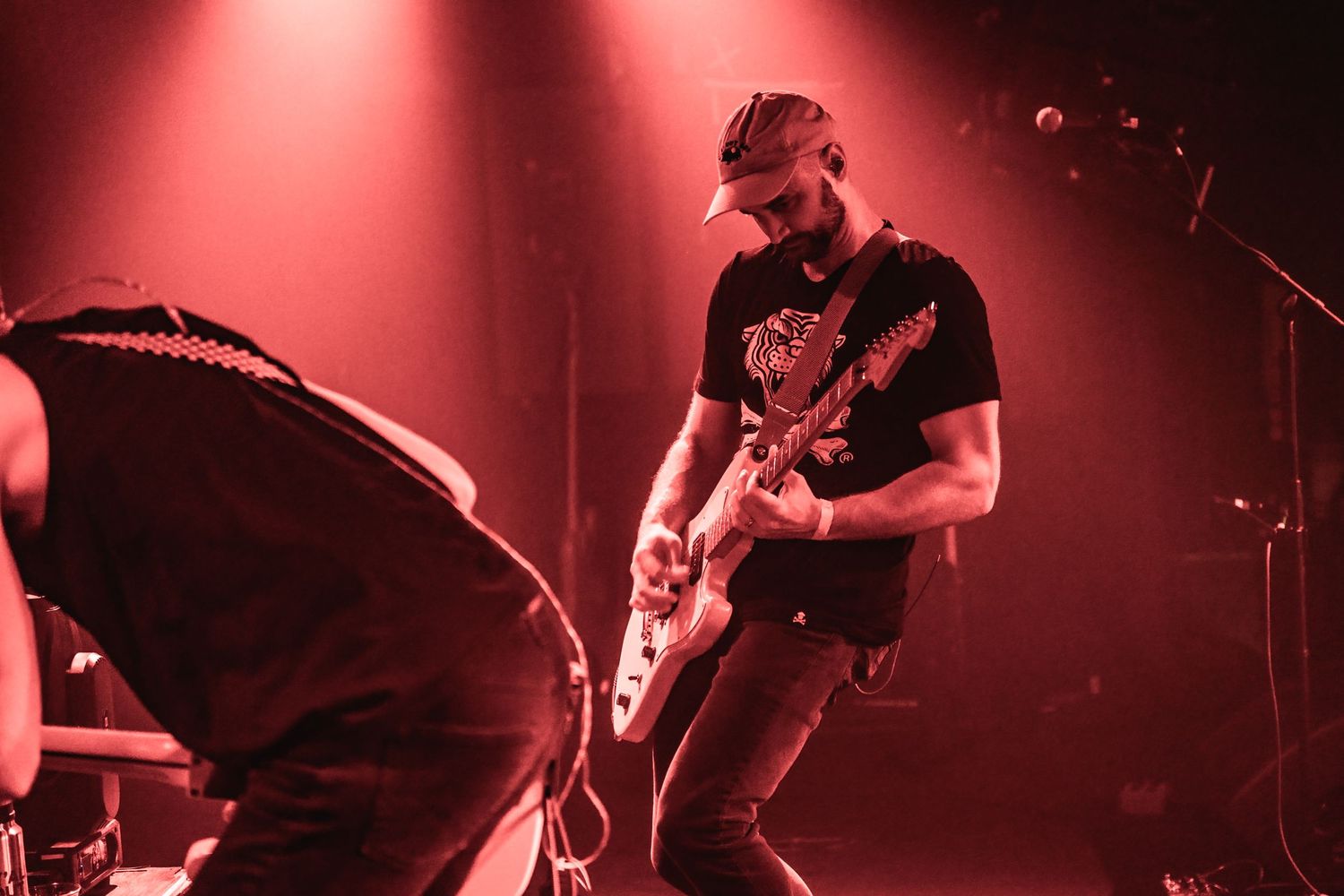 Guitarist plays on stage under dramatic red spotlights during live performance.