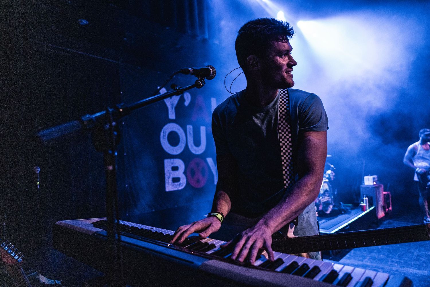 Musician plays keyboard under moody blue stage lighting during live performance.