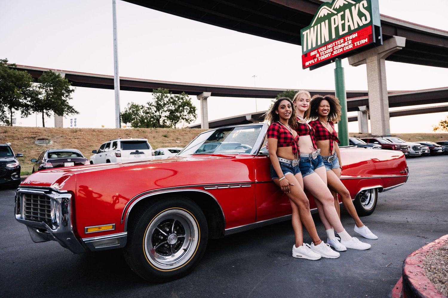 Group leaning against vintage red Cadillac at Twin Peaks parking lot.