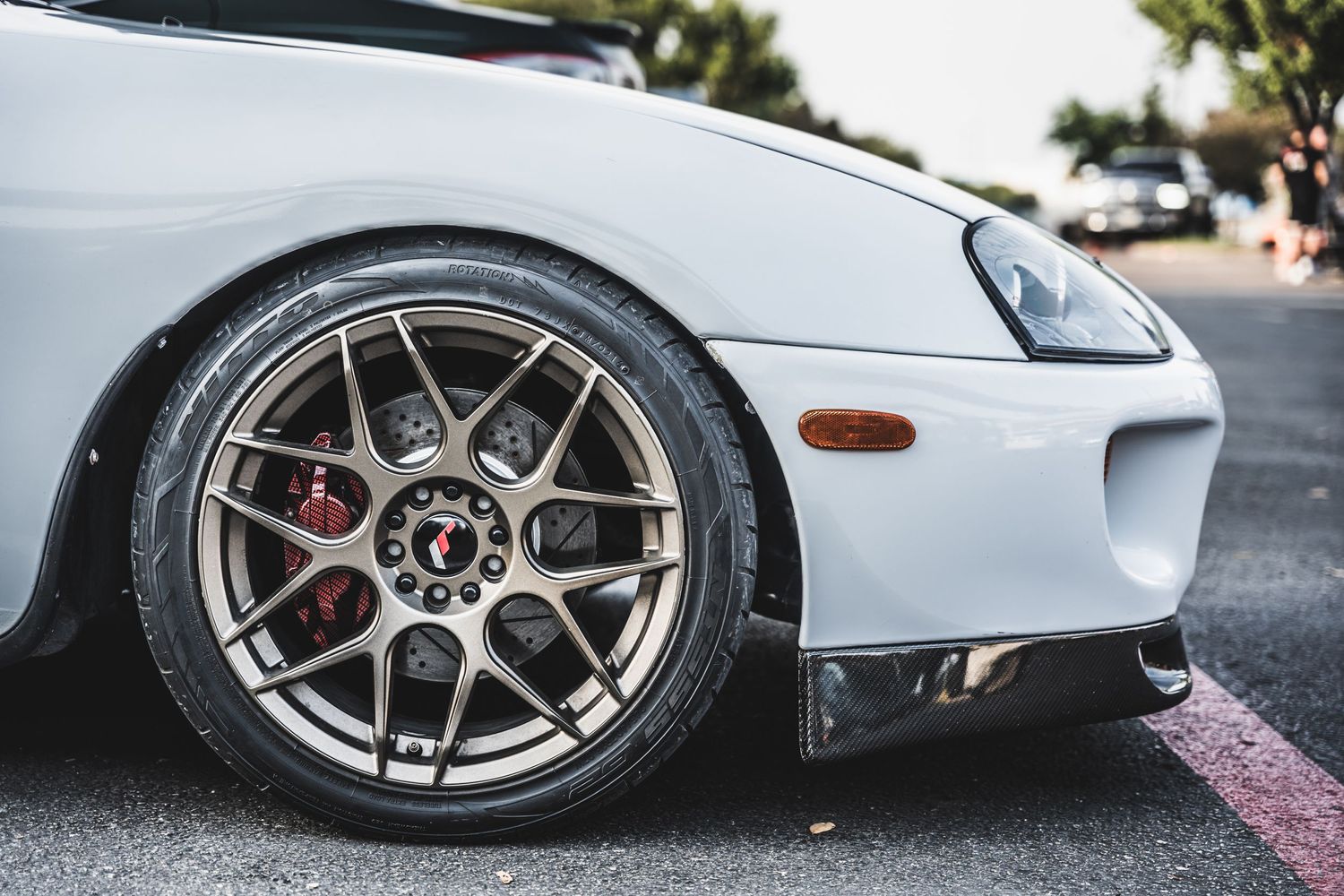 Close-up of a white sports car's custom wheel with red brake caliper.