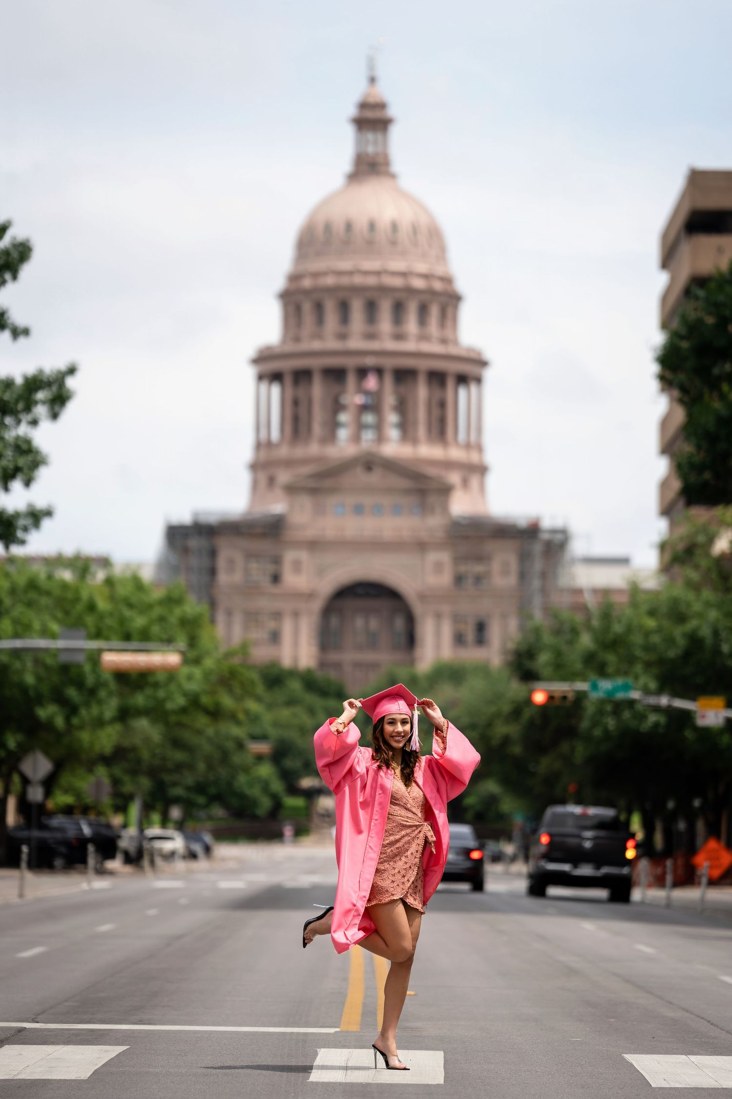 Graduate in pink robe poses in front of Texas State Capitol building in Austin.