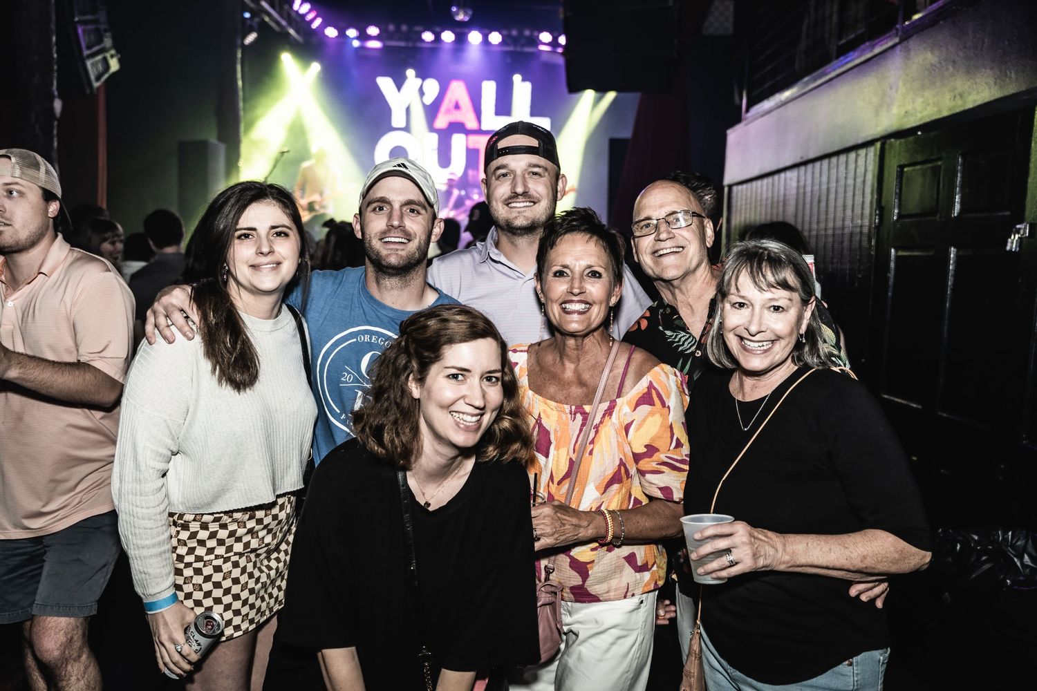 Group photo of concert attendees gathered under Y'ALL OUT stage lighting.