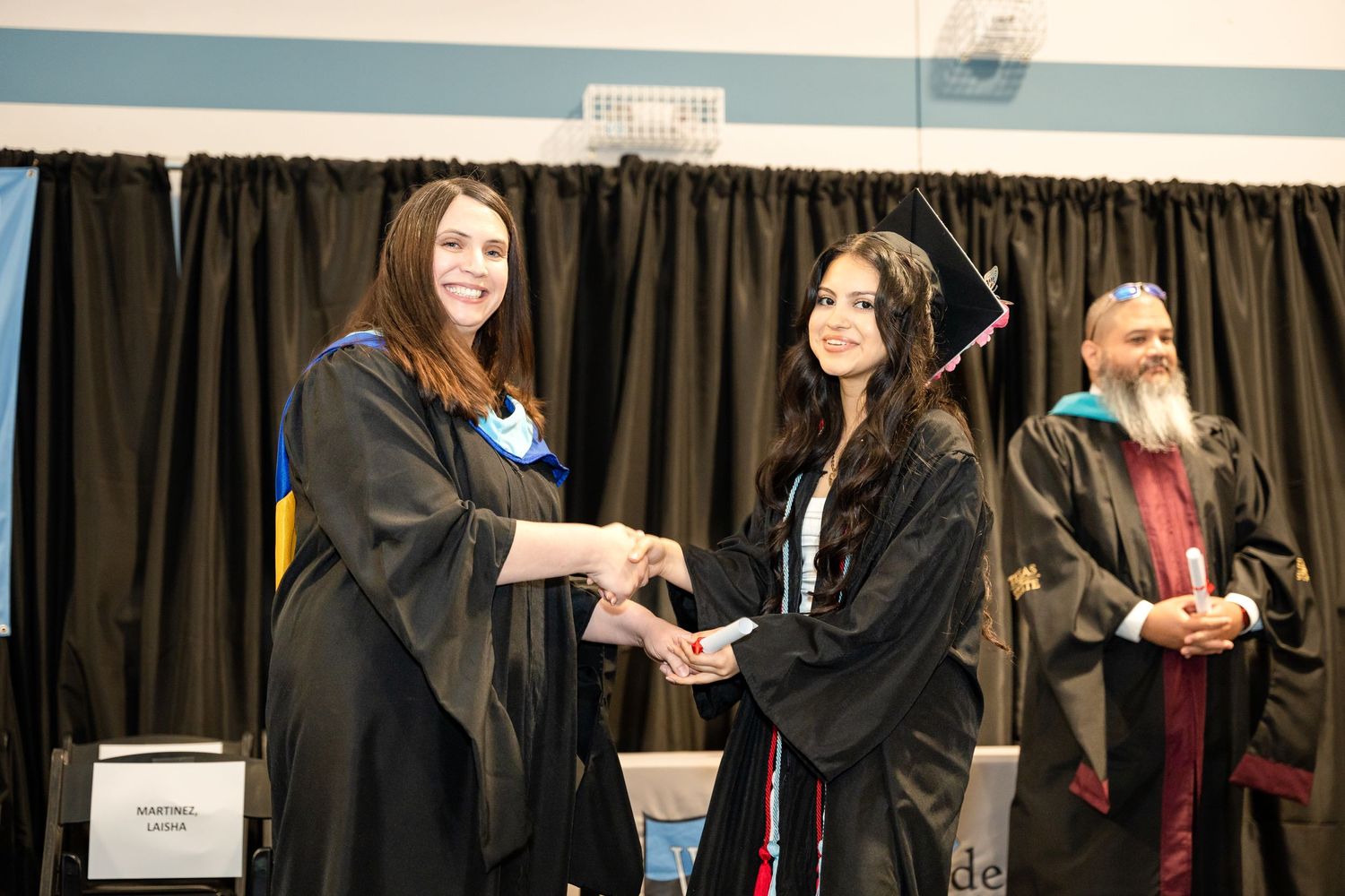 Graduate receiving diploma during commencement ceremony on stage.