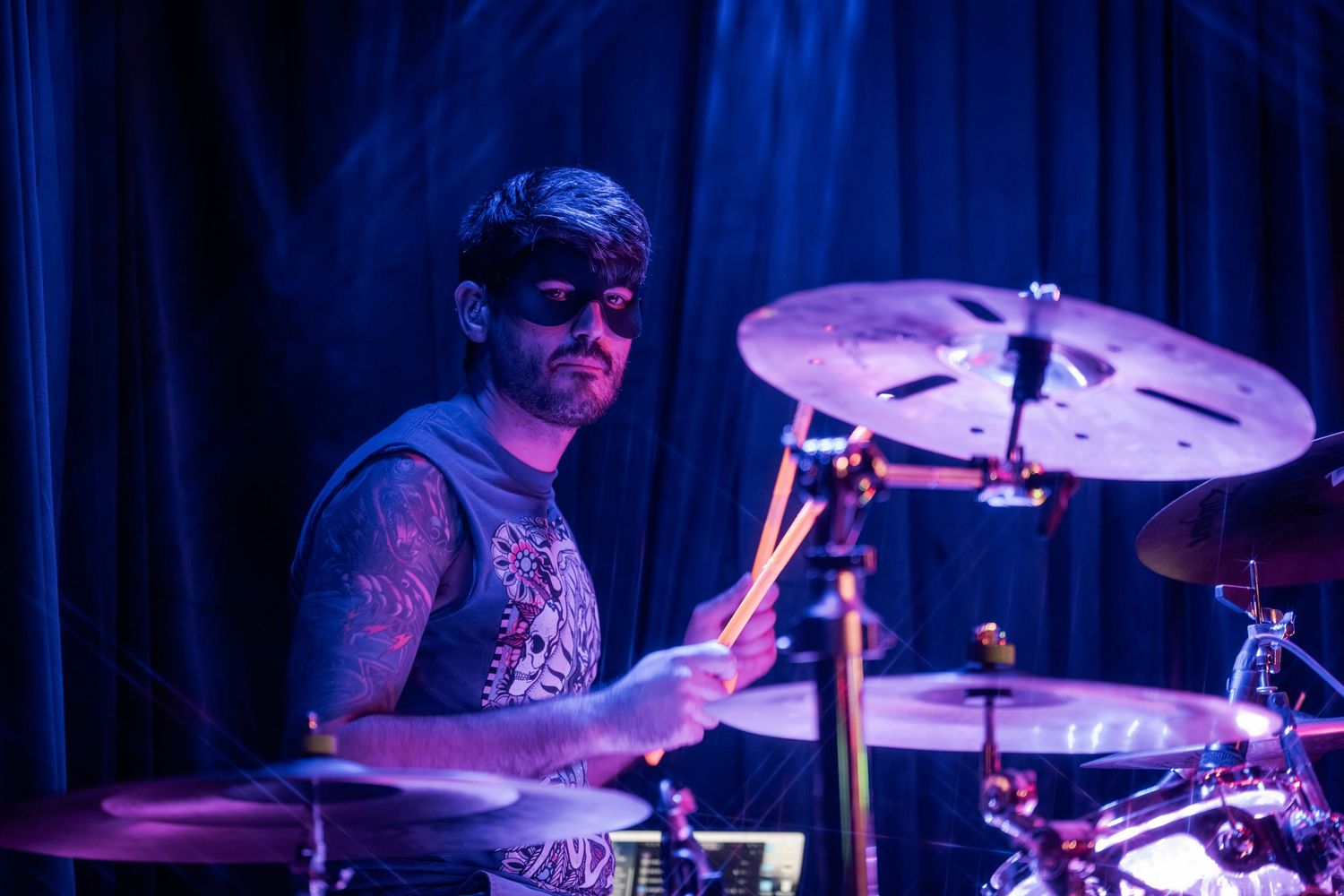 Drummer performing on stage with dramatic purple and blue lighting during a live concert performance.